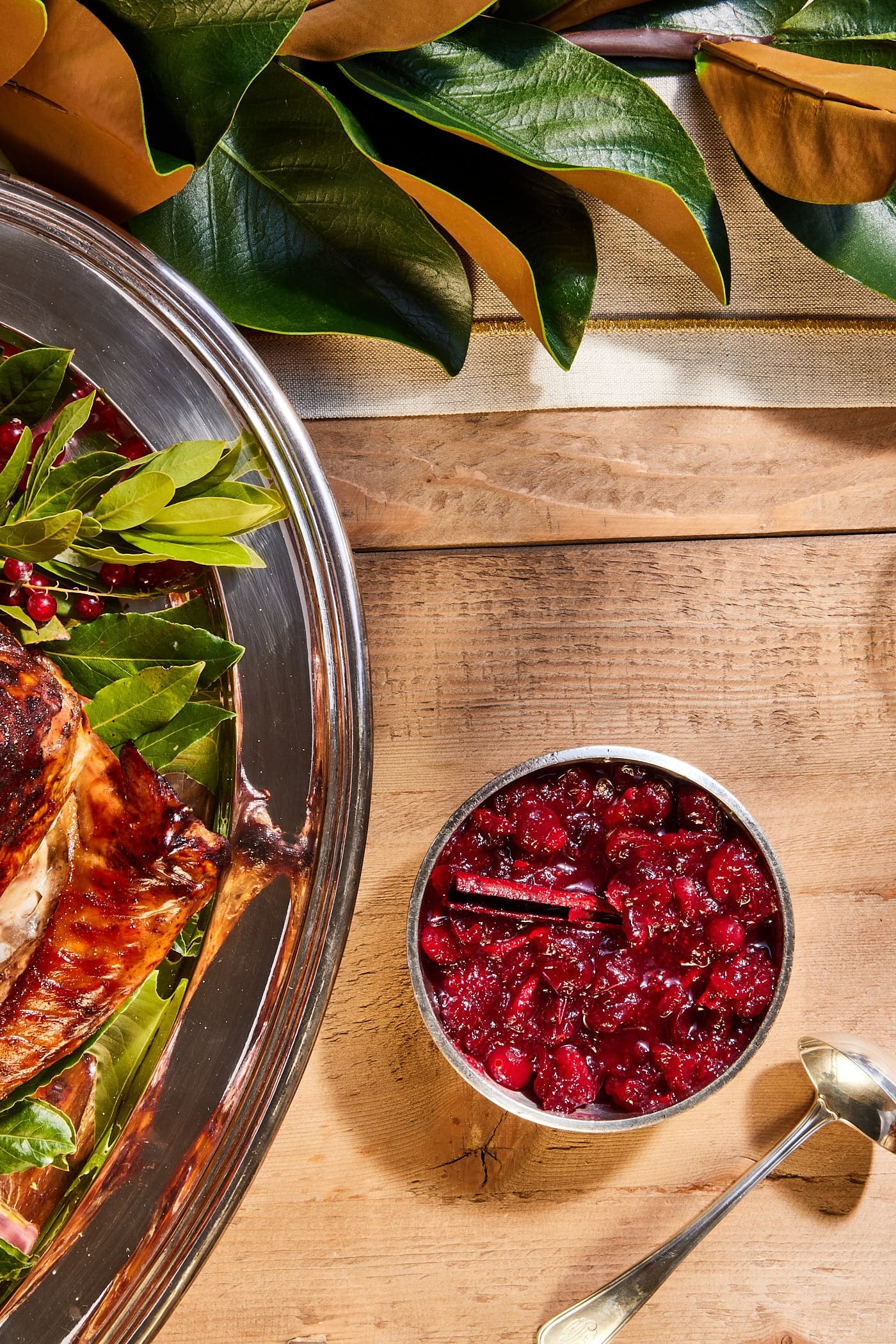 Wood surface with silver bowl filled with cranberry marmalade with turkey alongside.