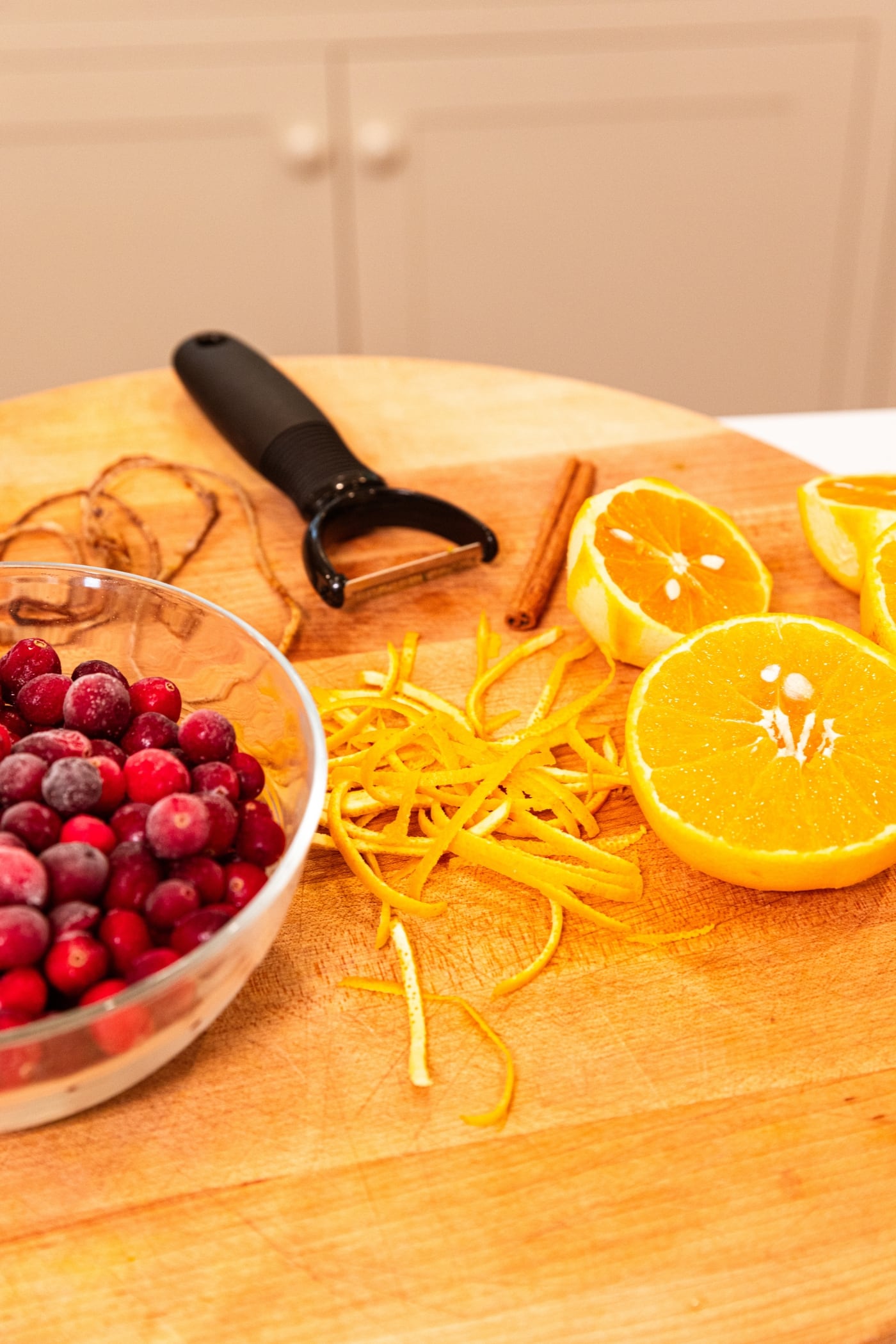 Strips of peeled orange zest with zester right behind all on wood cutting board.