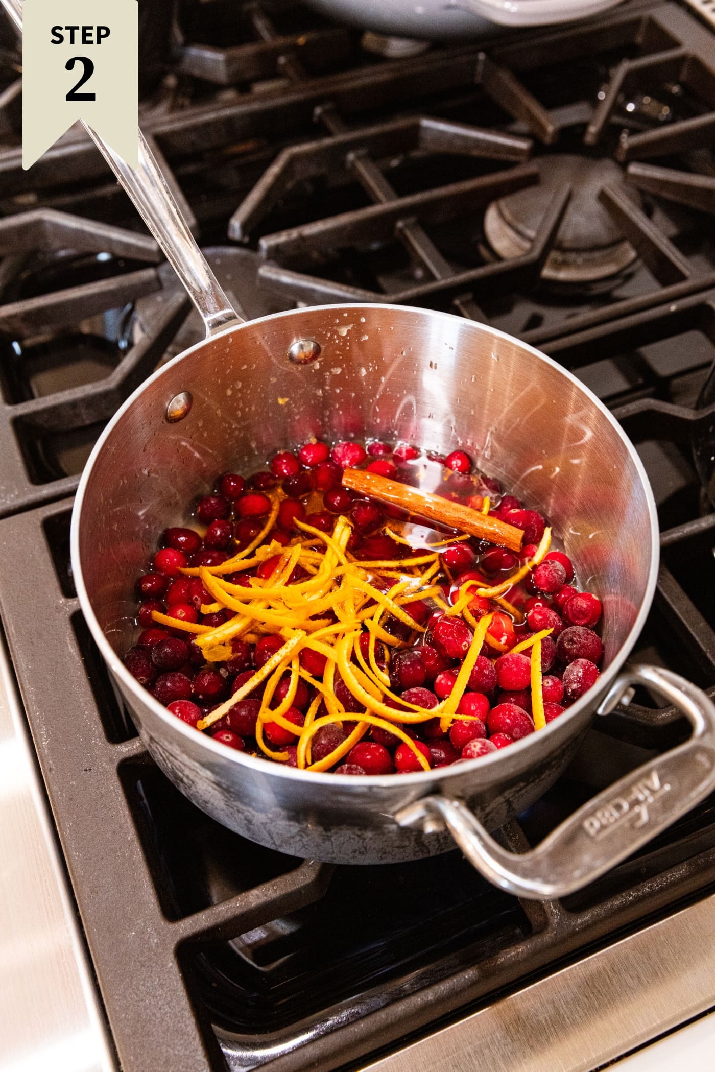 Metal saucepan filled with cranberries and strips of peeled orange zest before being cooked.