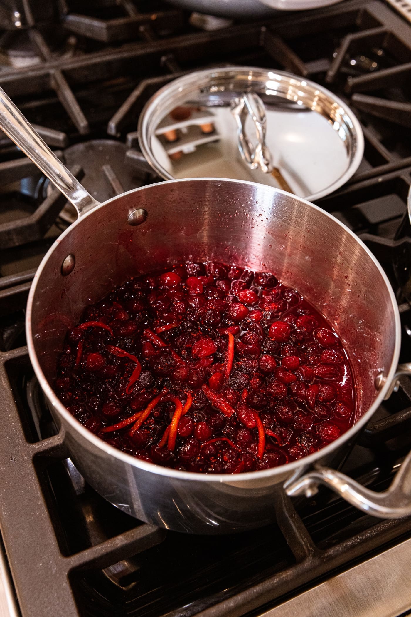 Metal saucepan filled with cooked cranberry marmalade with bits of strips of orange zest.