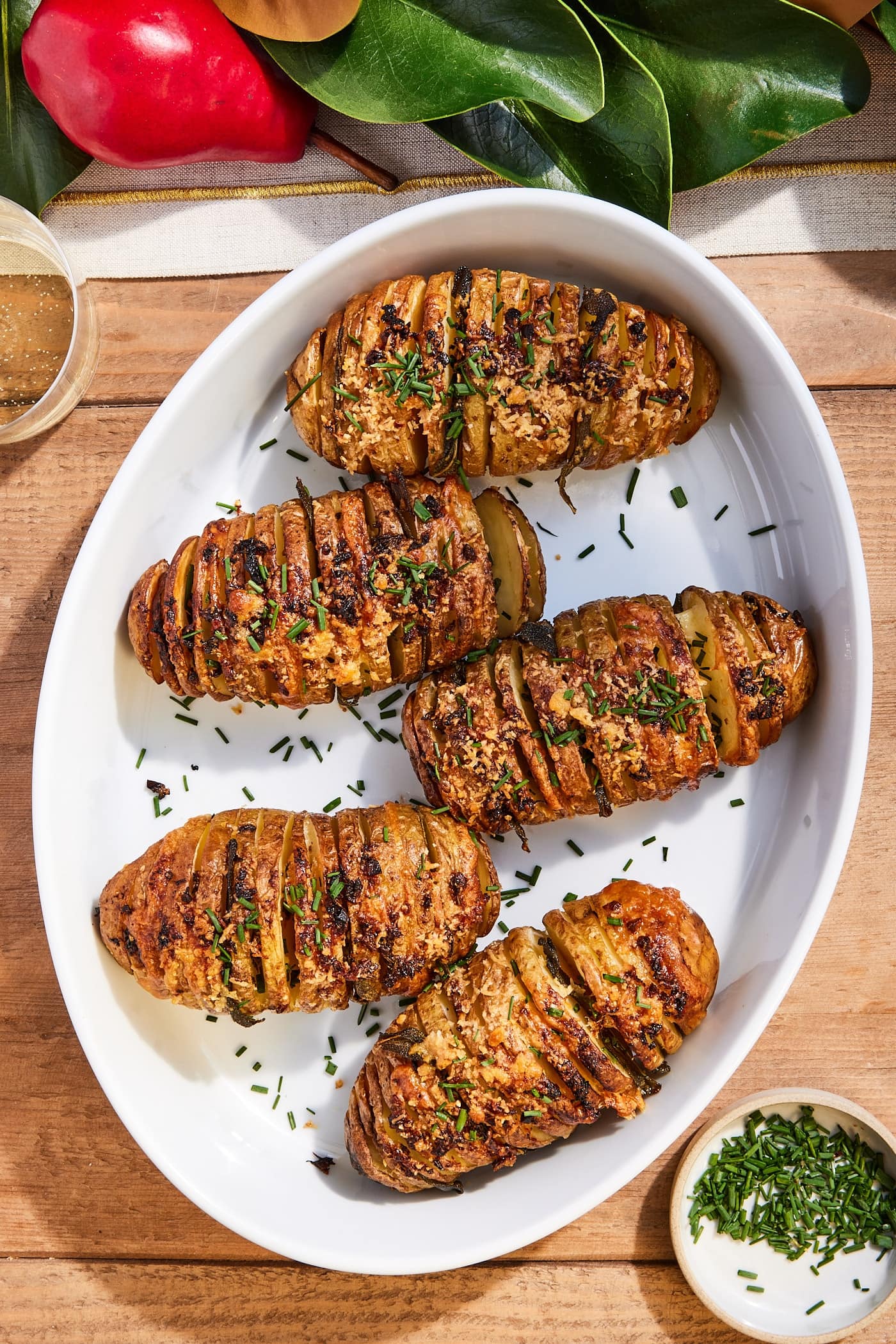 White baking dish with Hasselback potatoes after roasting in the oven topped with freshly chopped chives on wood table.