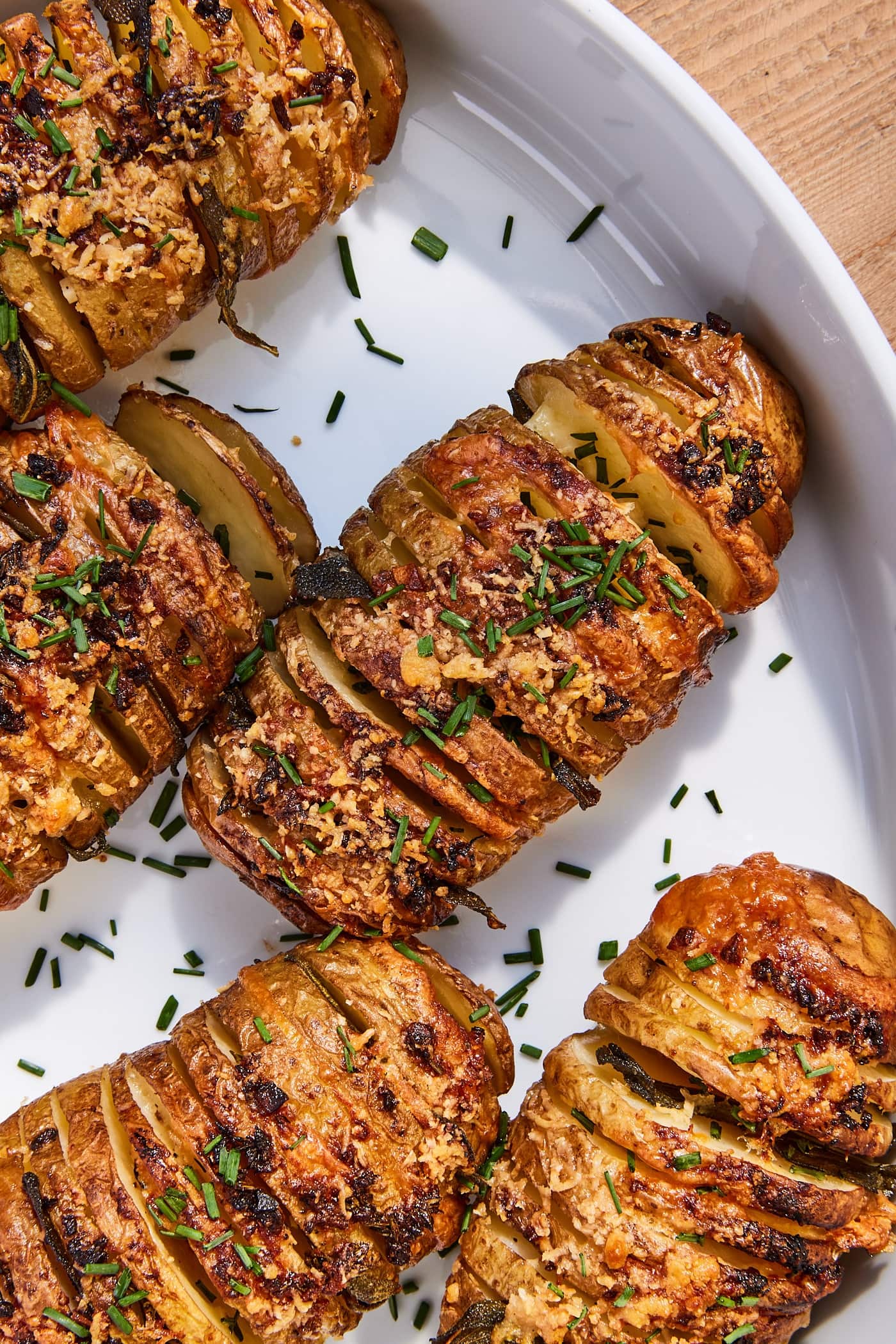 Sliced Hasselback potatoes with garlic butter topping sitting in white baking dish with fresh chives chopped on top.