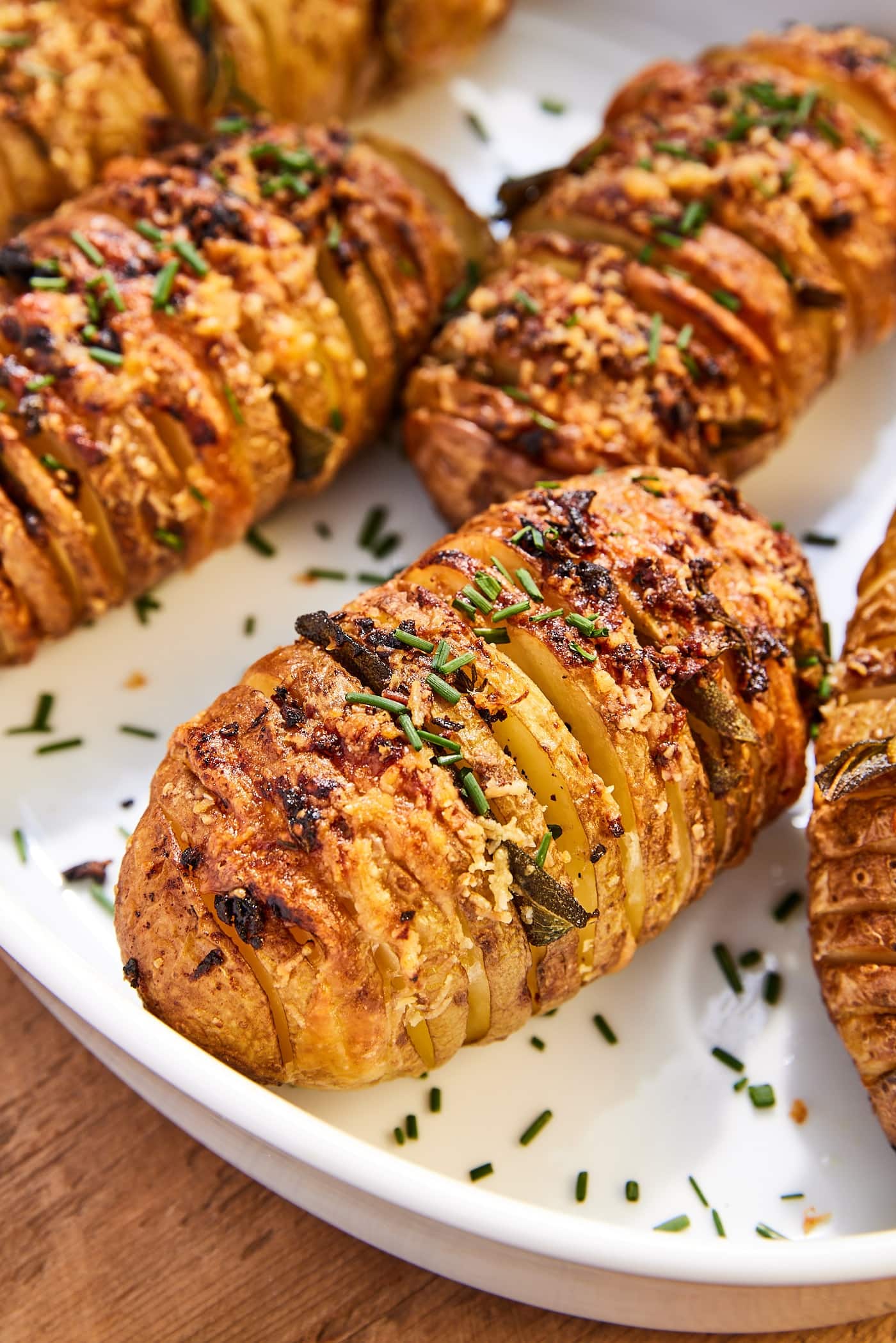 Hasselback potatoes with garlic butter topping in white baking dish topped with fresh chives.