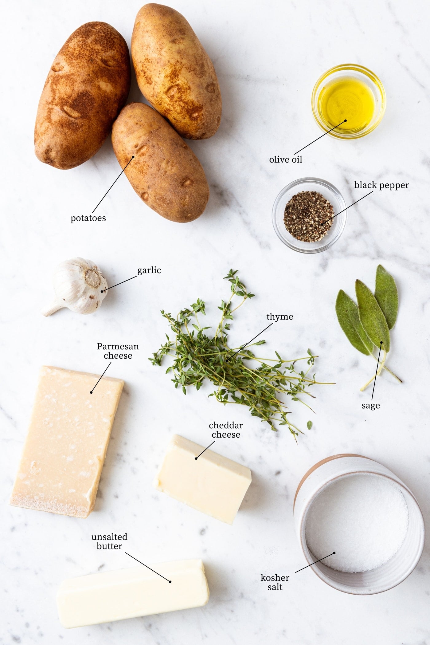 White marble surface filled with all ingredients needed to make garlic butter Hasselback potatoes including potatoes, herbs, salt, olive oil, cheese, and more.