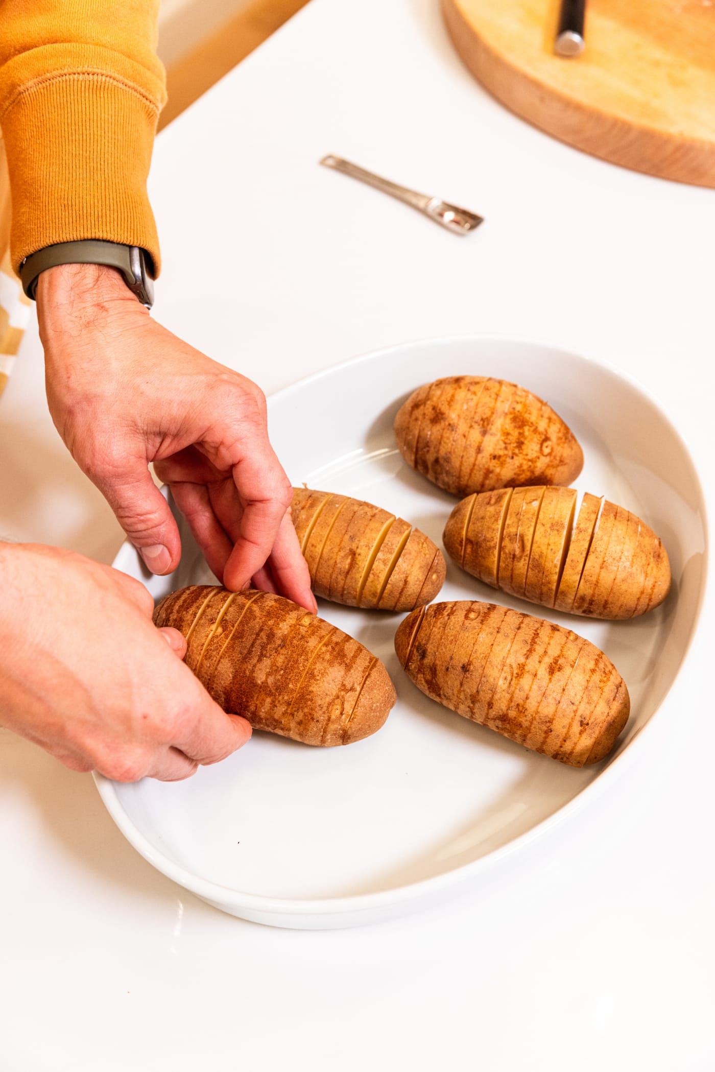 Hand arranging sliced Hasselback potatoes in a white baking dish before putting in the oven to roast.