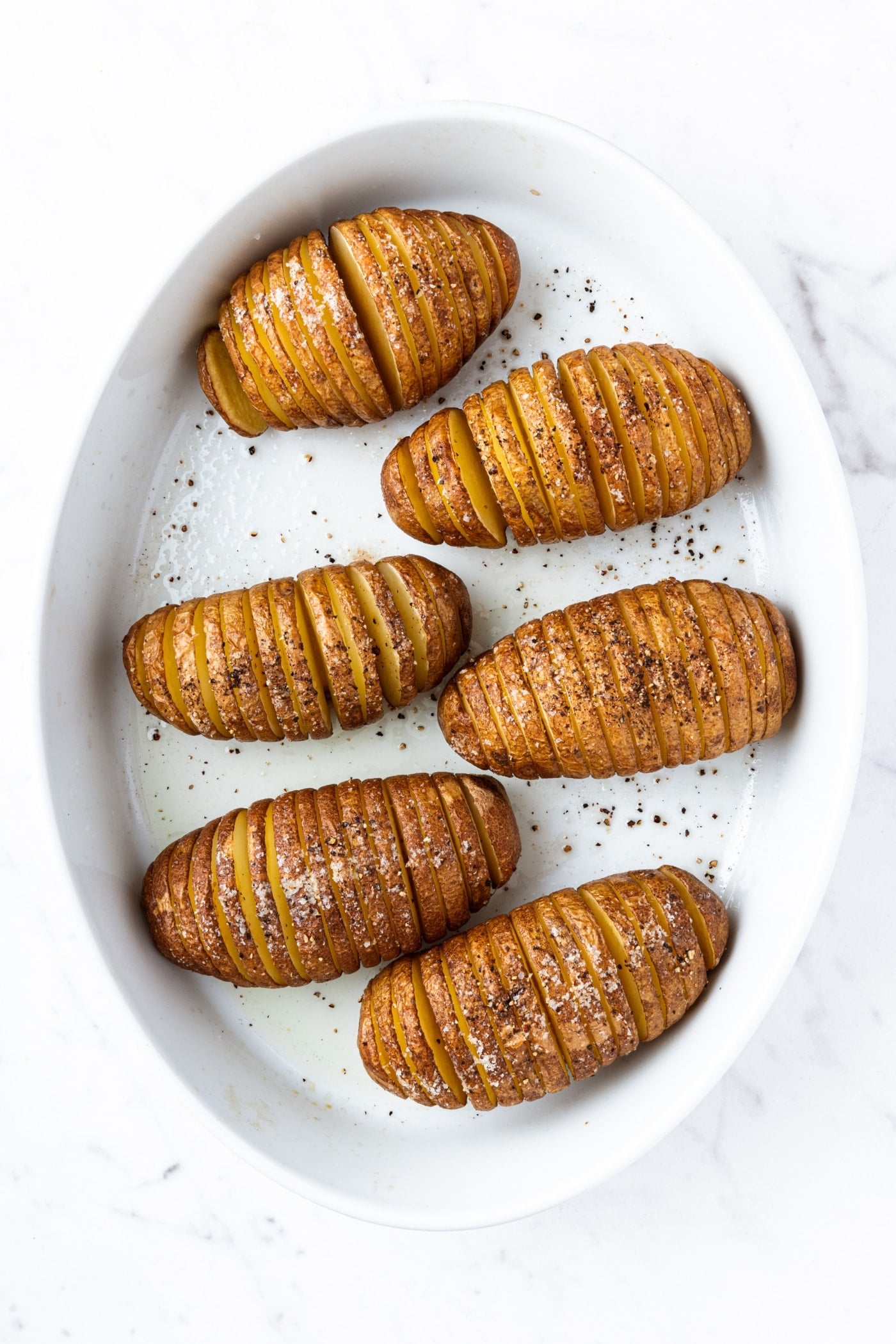 Hasselback potatoes in a white baking dish right after coming out of the oven after roasting.