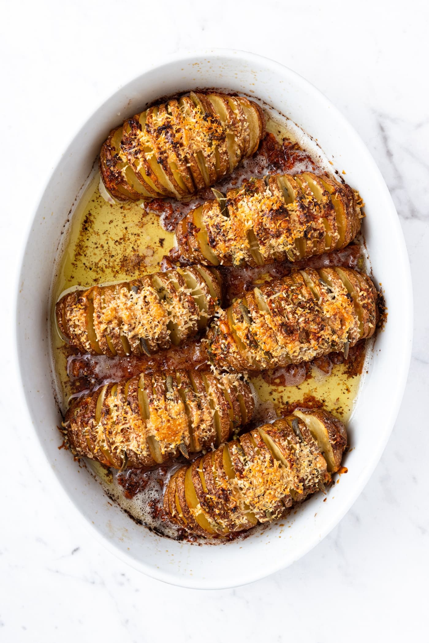 Hasselback potatoes right after coming out of the oven with browned cheese on top and garlic butter in bottom of the pan.