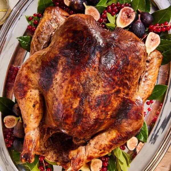 Large silver platter resting on wooden table with browned turkey resting before being sliced for Thanksgiving.
