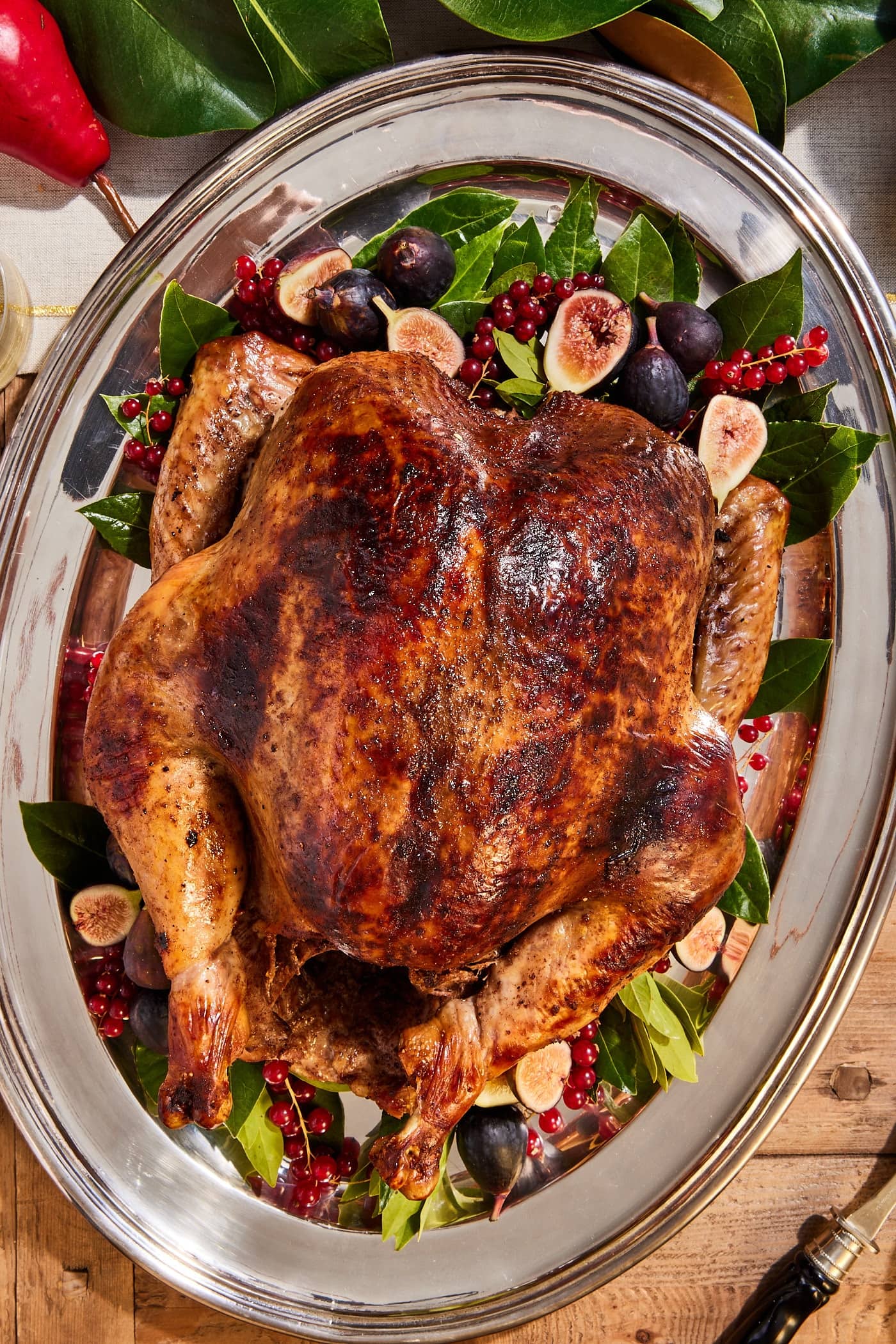 Golden brown orange spiced turkey resting on a silver serving platter with figs and bay leaves underneath.