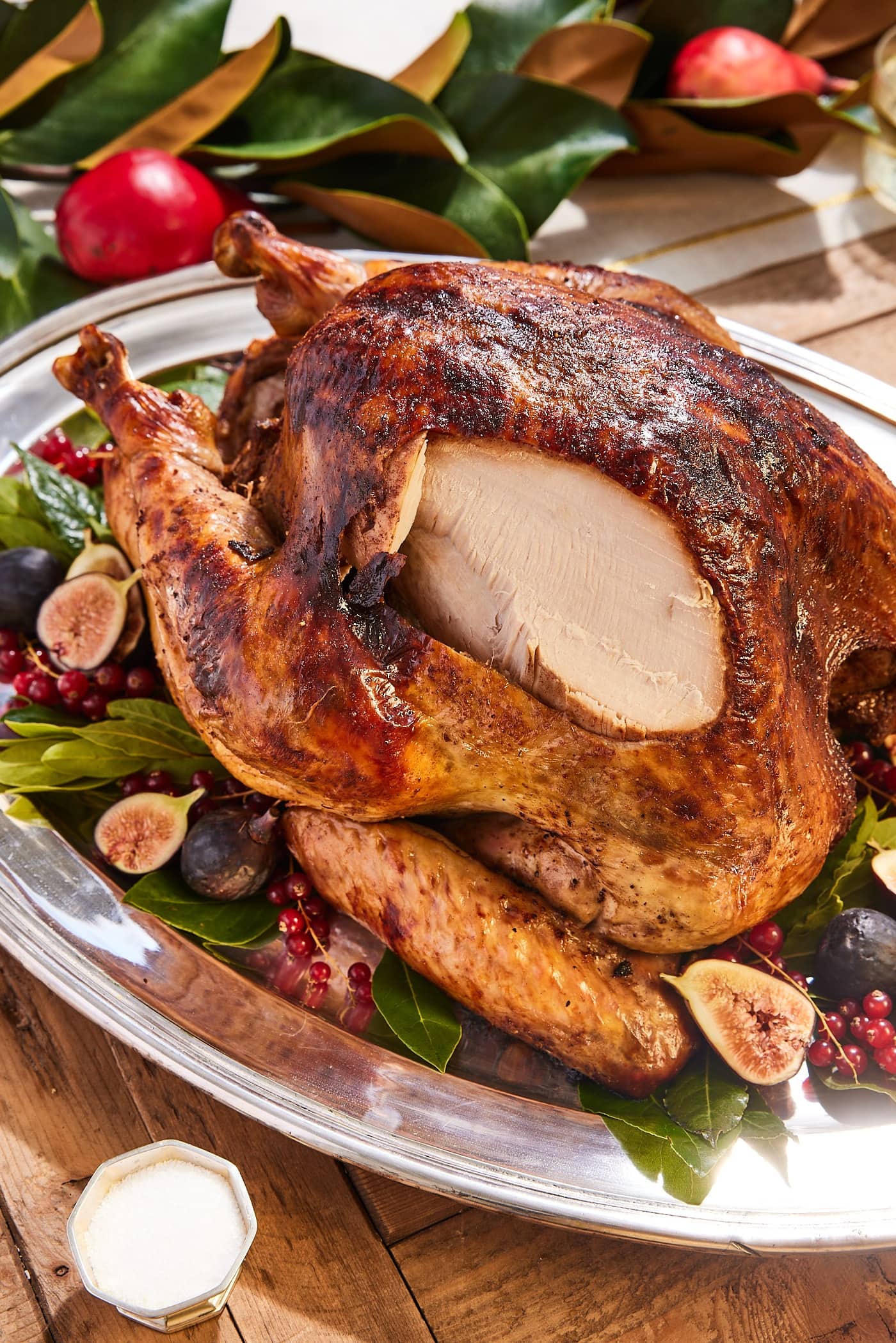 Large browned turkey sitting on a silver platter with a slice taken out from the side of the turkey showing interior white breast meat.
