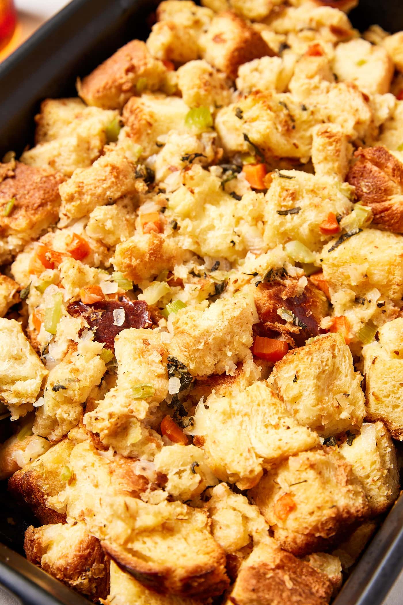 Baked cubes of toasted bread in black baking pan to form traditional stuffing with pieces of cooked vegetable.