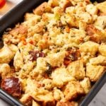 Large black baking pan filled with baked traditional stuffing with pieces of vegetables on the top.