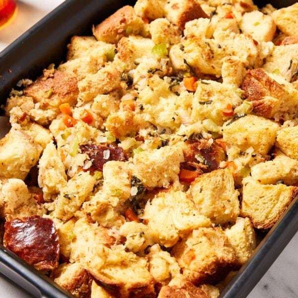 Large black baking pan filled with baked traditional stuffing with pieces of vegetables on the top.