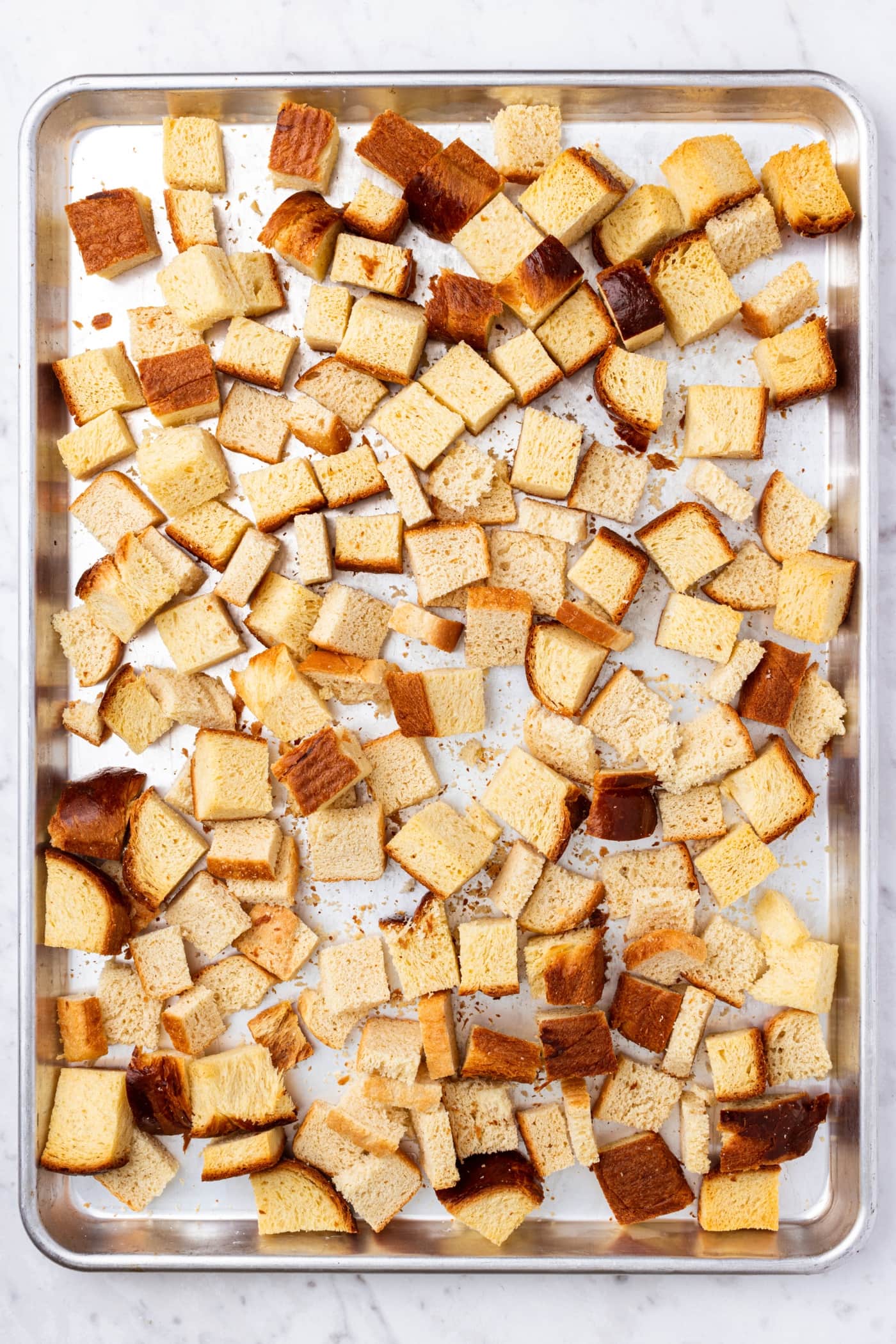 Toasted cubes of bread resting on a metal baking sheet right after coming out of the oven.