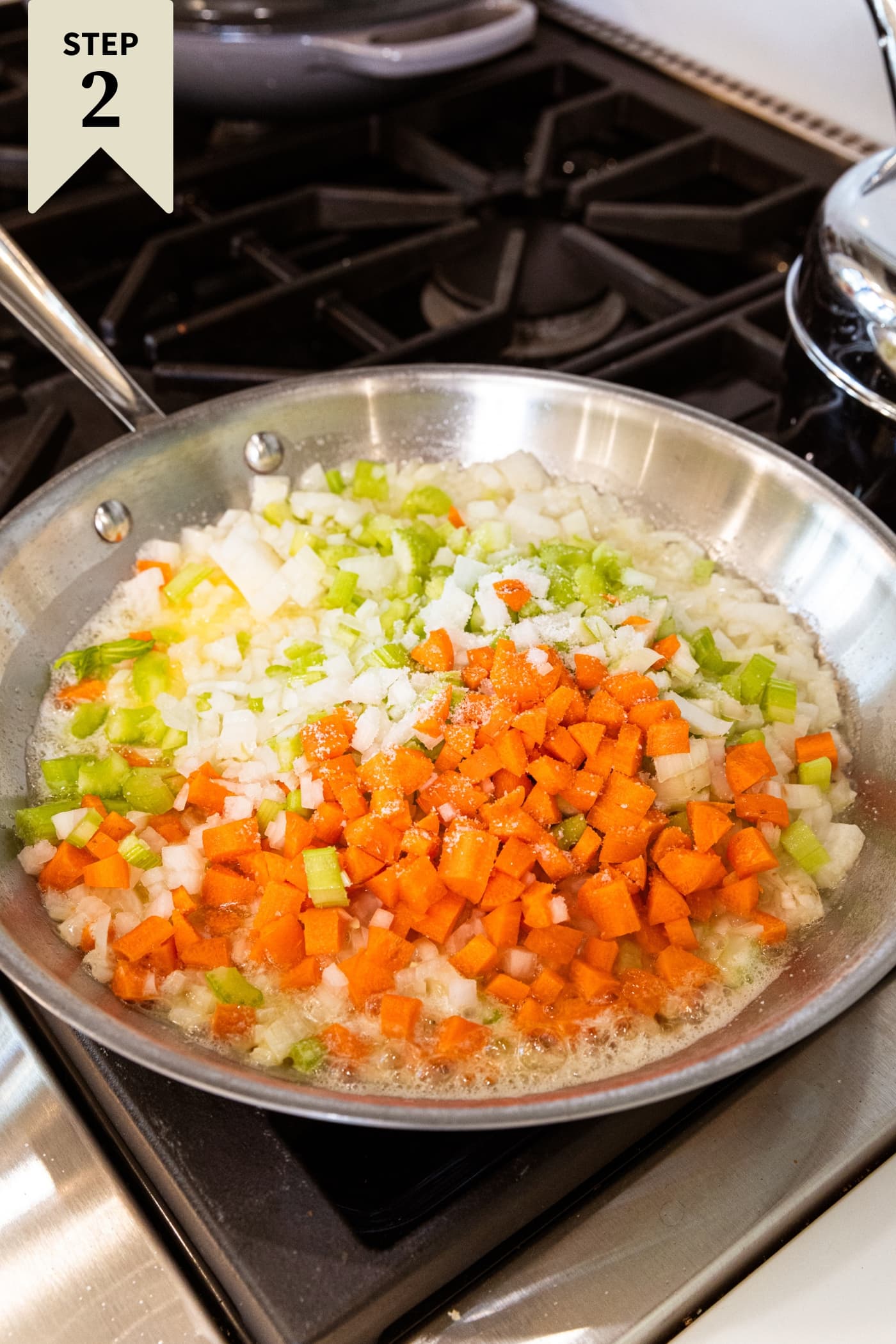 Large metal skillet with chopped vegetables cooking melting butter on the stovetop.