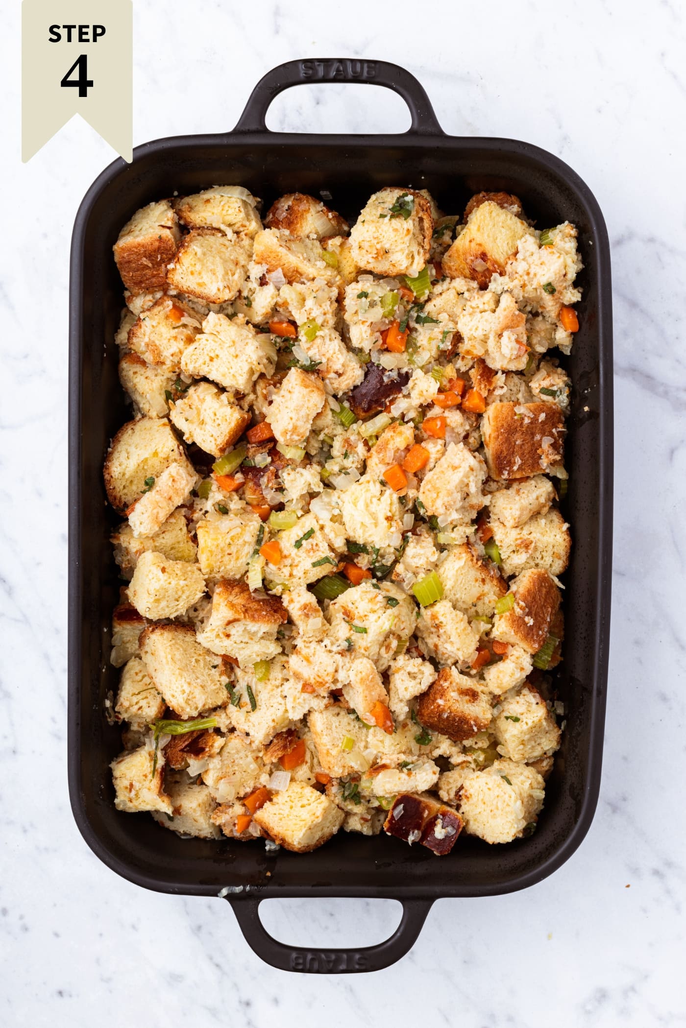 Black baking pan filled with unbaked traditional stuffing with vegetables on top.
