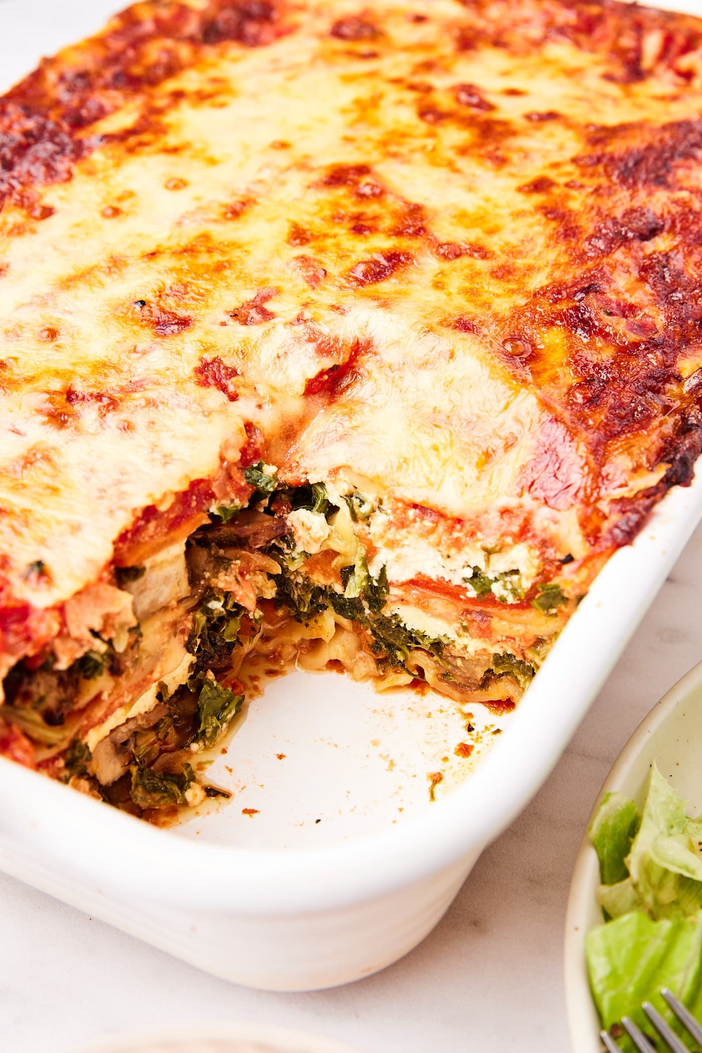 White rectangular baking dish filled with layers of vegetable lasagna with spinach, mushrooms, and more.