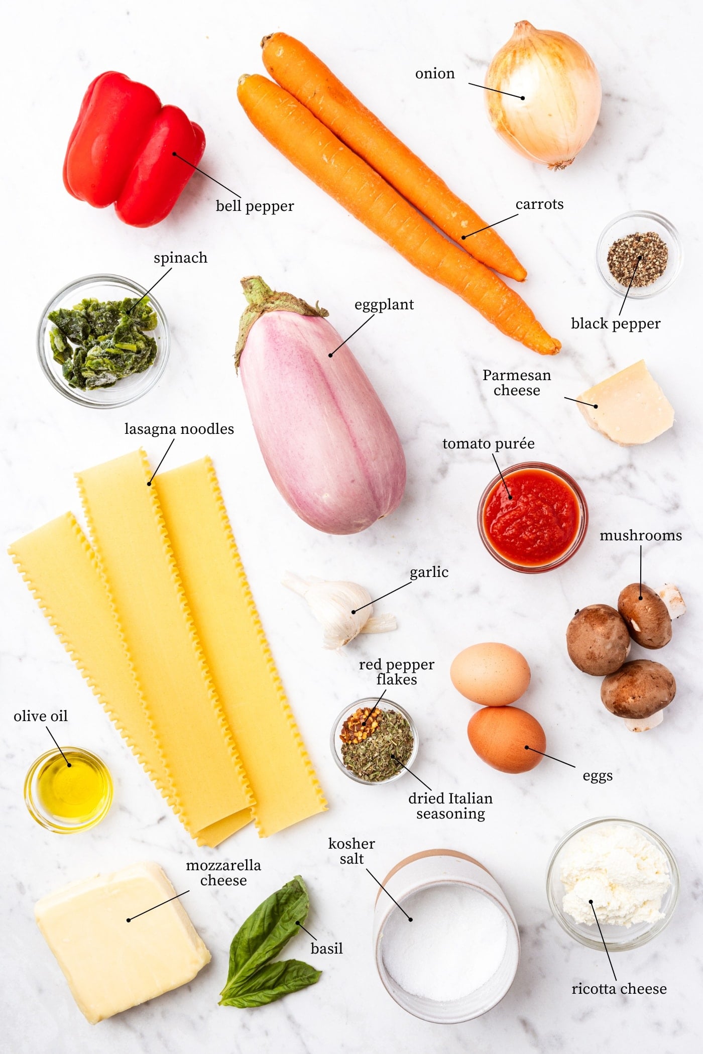 White marble surface filled with all ingredients needed to prepare vegetable lasagna including noodles, vegetables, spices, cheese, and more.