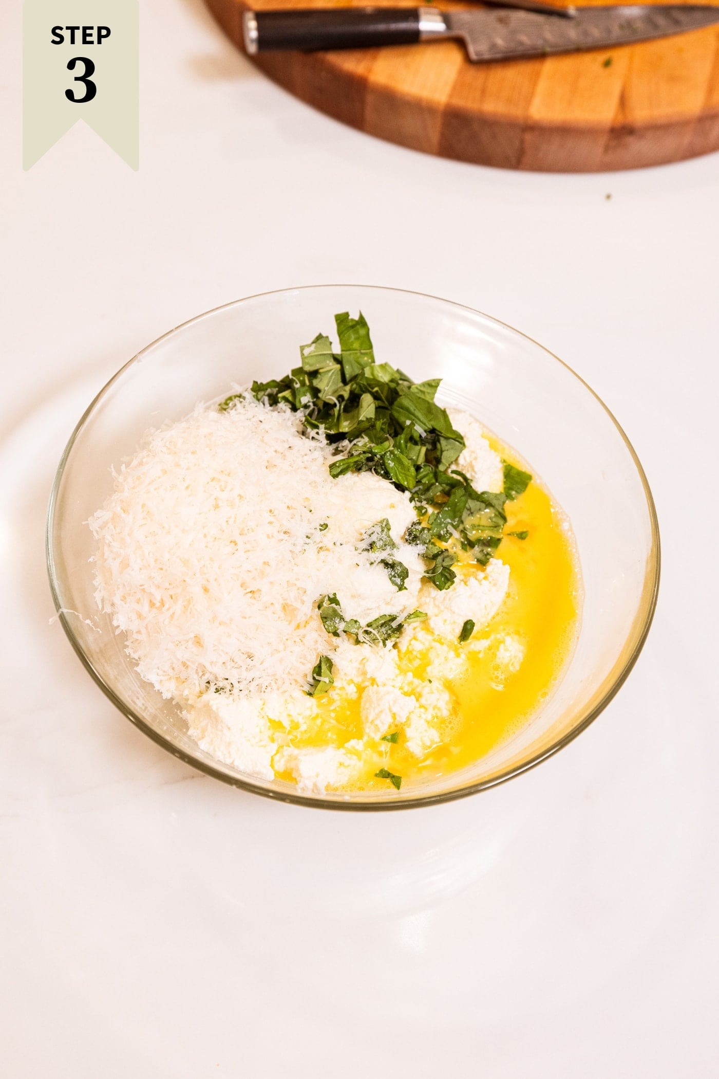 Glass bowl filled with all ingredients needed to make a ricotta filling for lasagna.