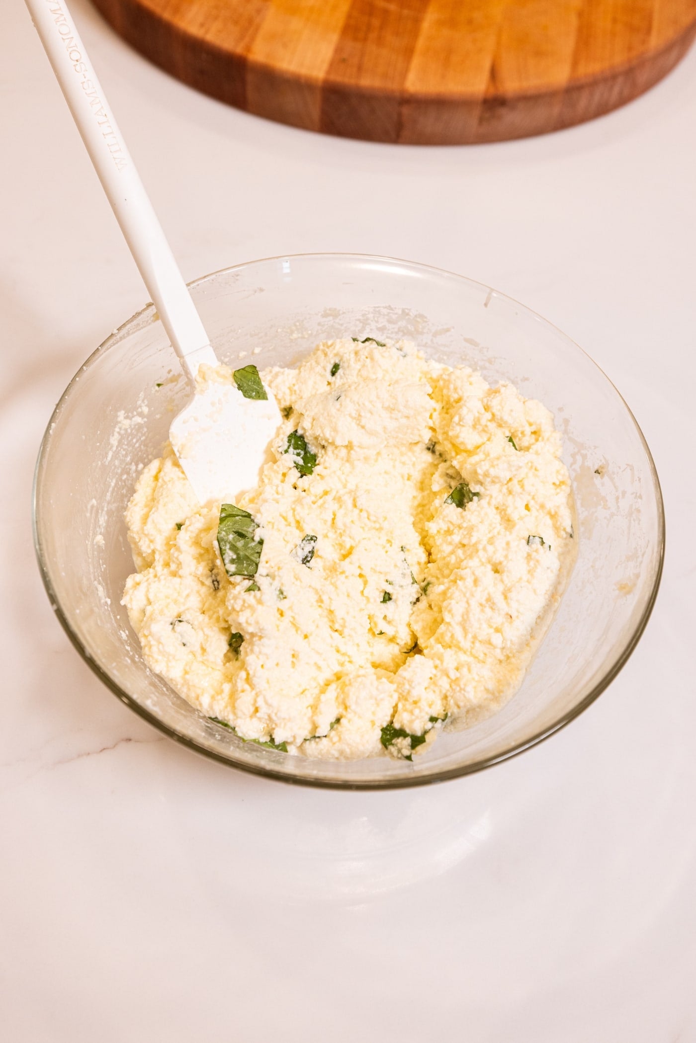 Glass bowl filled with ricotta filling after being mixed with white spatula.