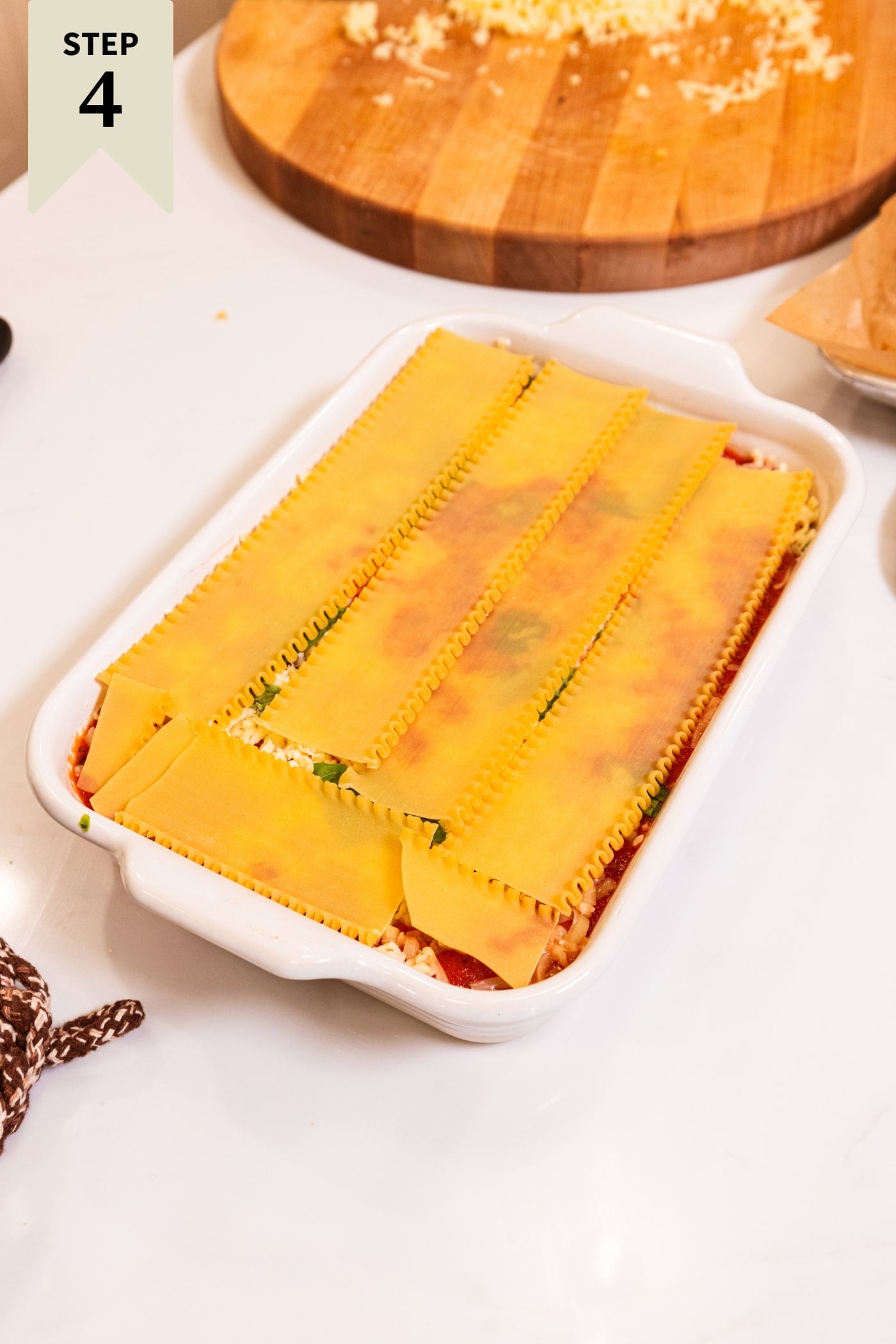 Uncooked noodles sitting on top of layers of lasagna in white baking dish.