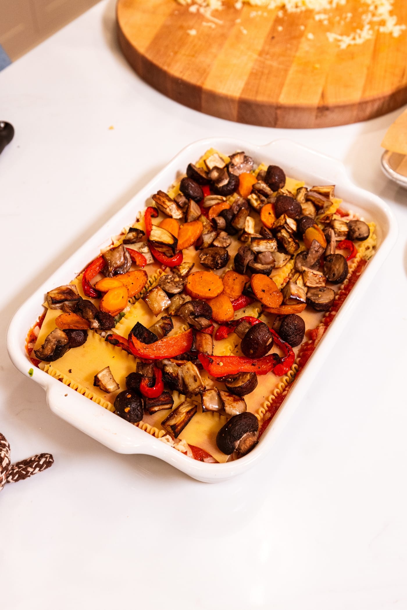 Roasted vegetables laying on top of raw lasagna noodles in a large baking dish to form vegetable lasagna.