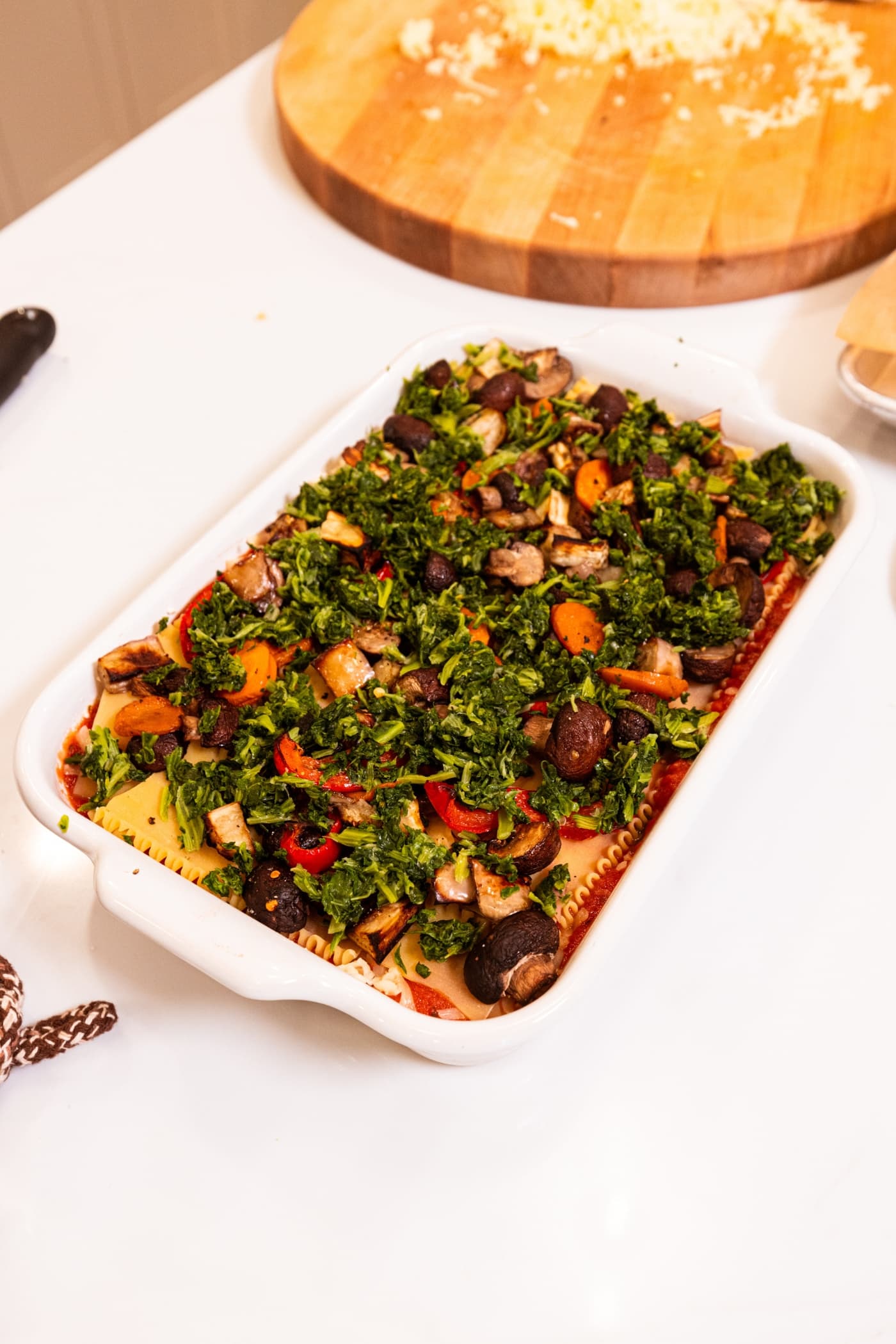 Frozen spinach layered on top of vegetables to form vegetable lasagna in a rectangular baking dish.
