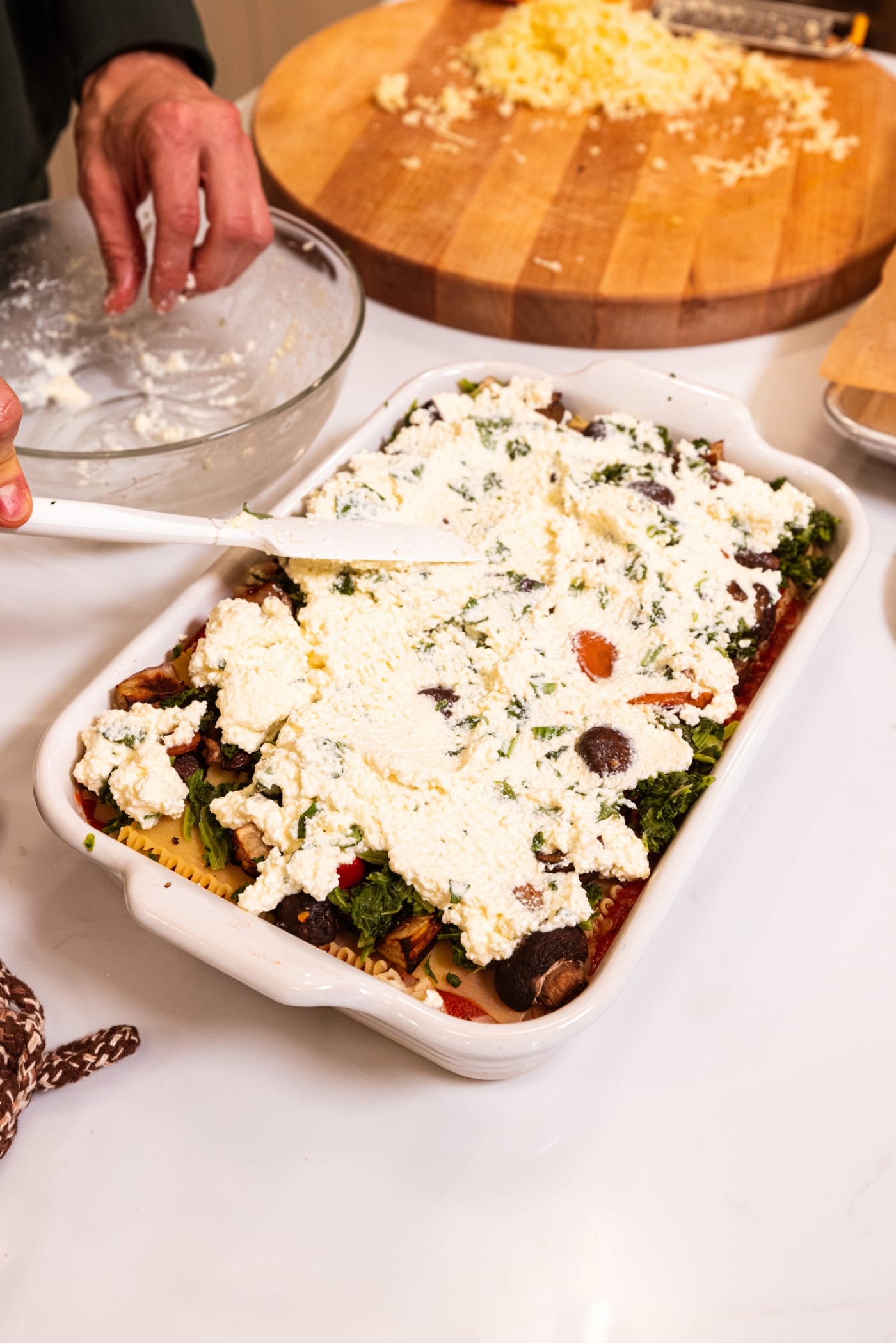 Ricotta mixture being spread on top of vegetables in white baking dish to make vegetable lasagna.