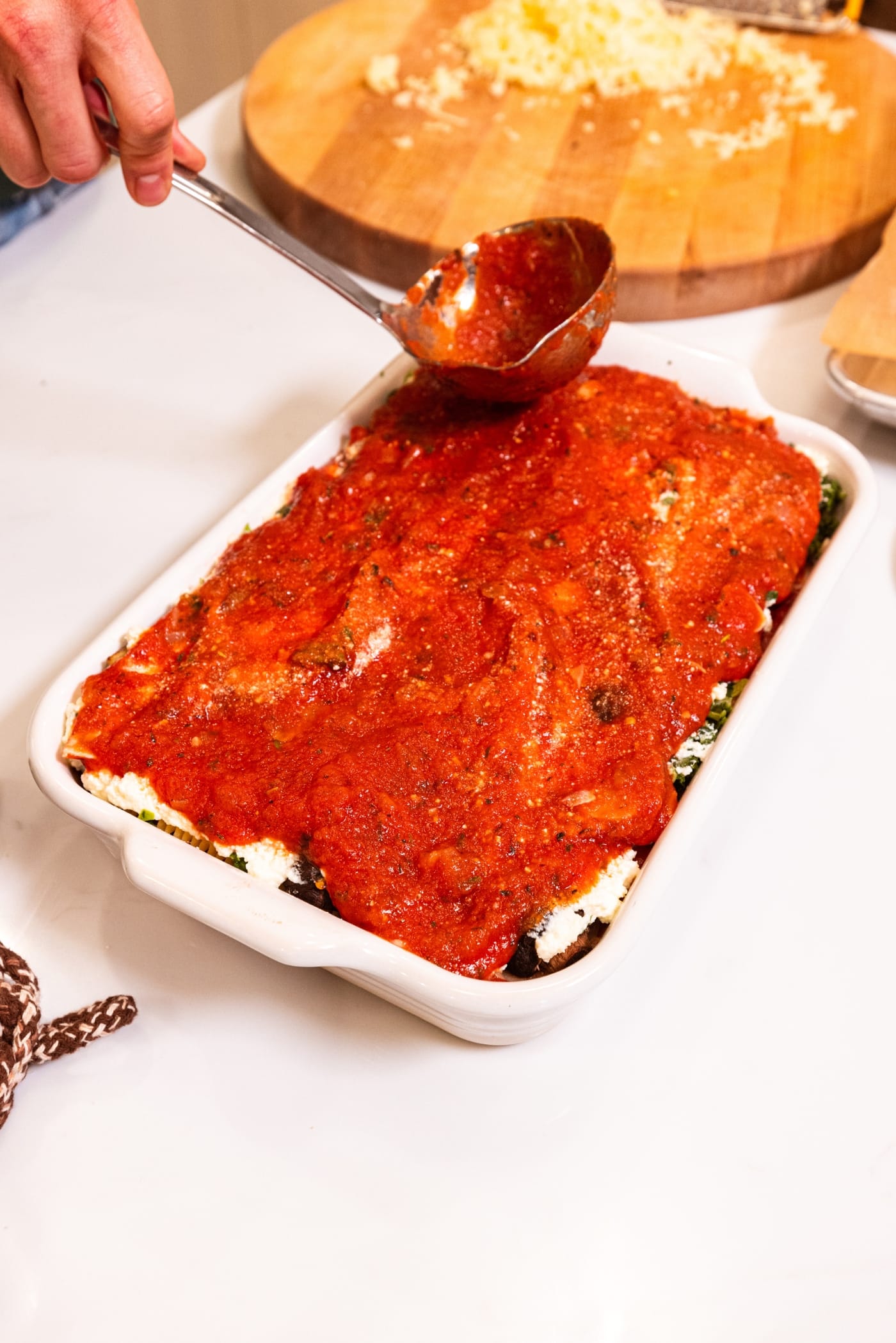 Tomato sauce being spread on the top of a full baking pan with layers of noodles to form vegetable lasagna.