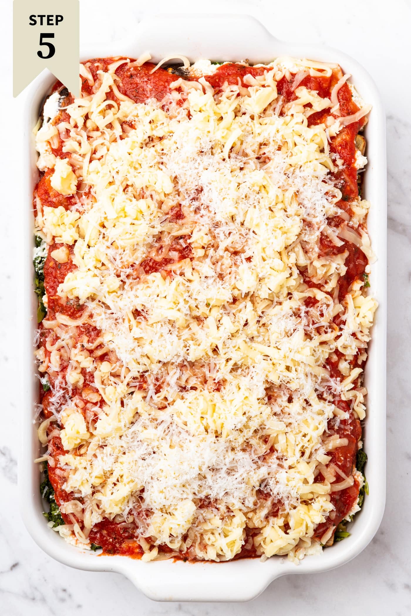 White baking dish filled with vegetable lasagna and shredded cheese on top right before going into the oven to bake.