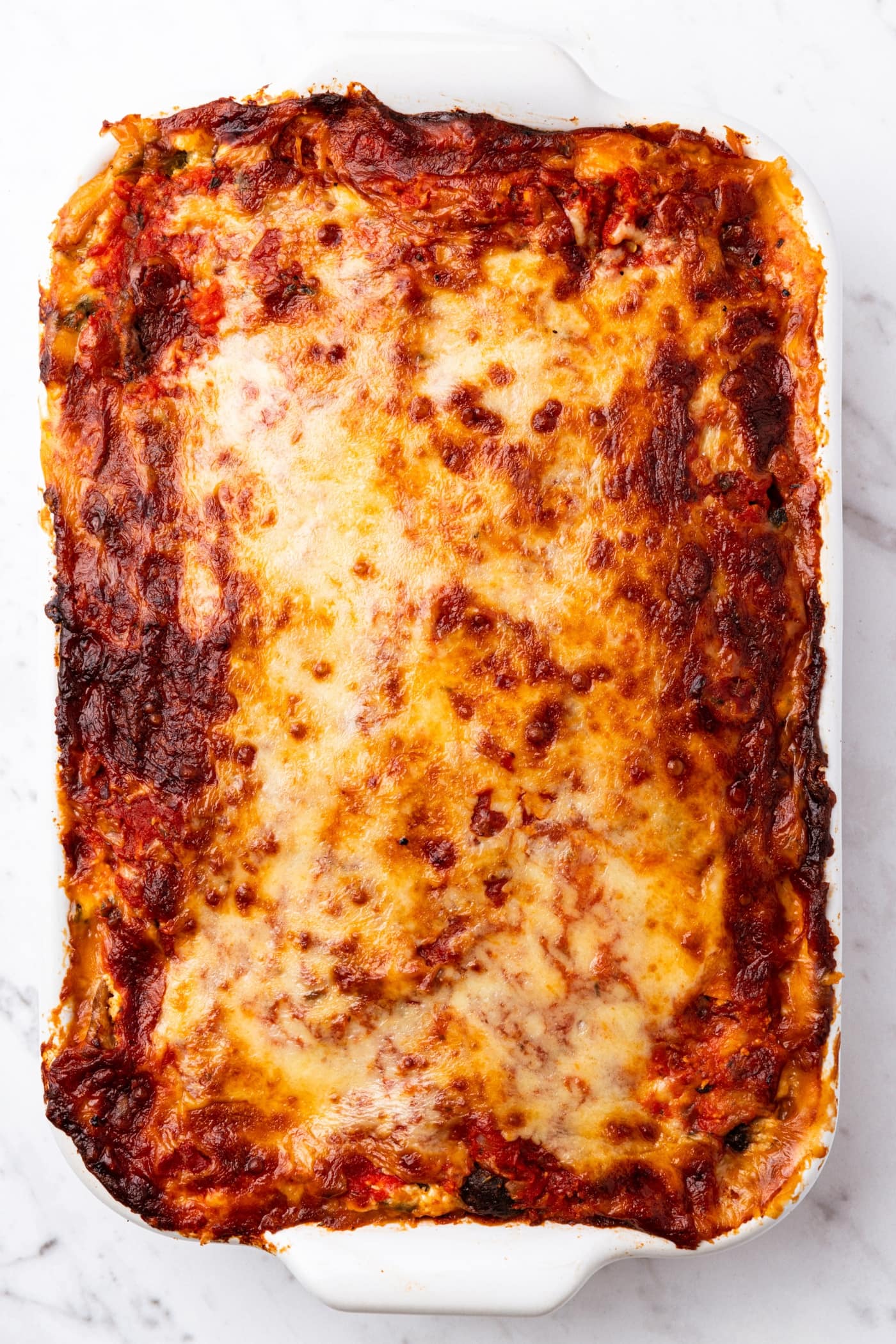 Rectangular white baking dish filled with freshly baked vegetable lasagna with melted cheese on top.