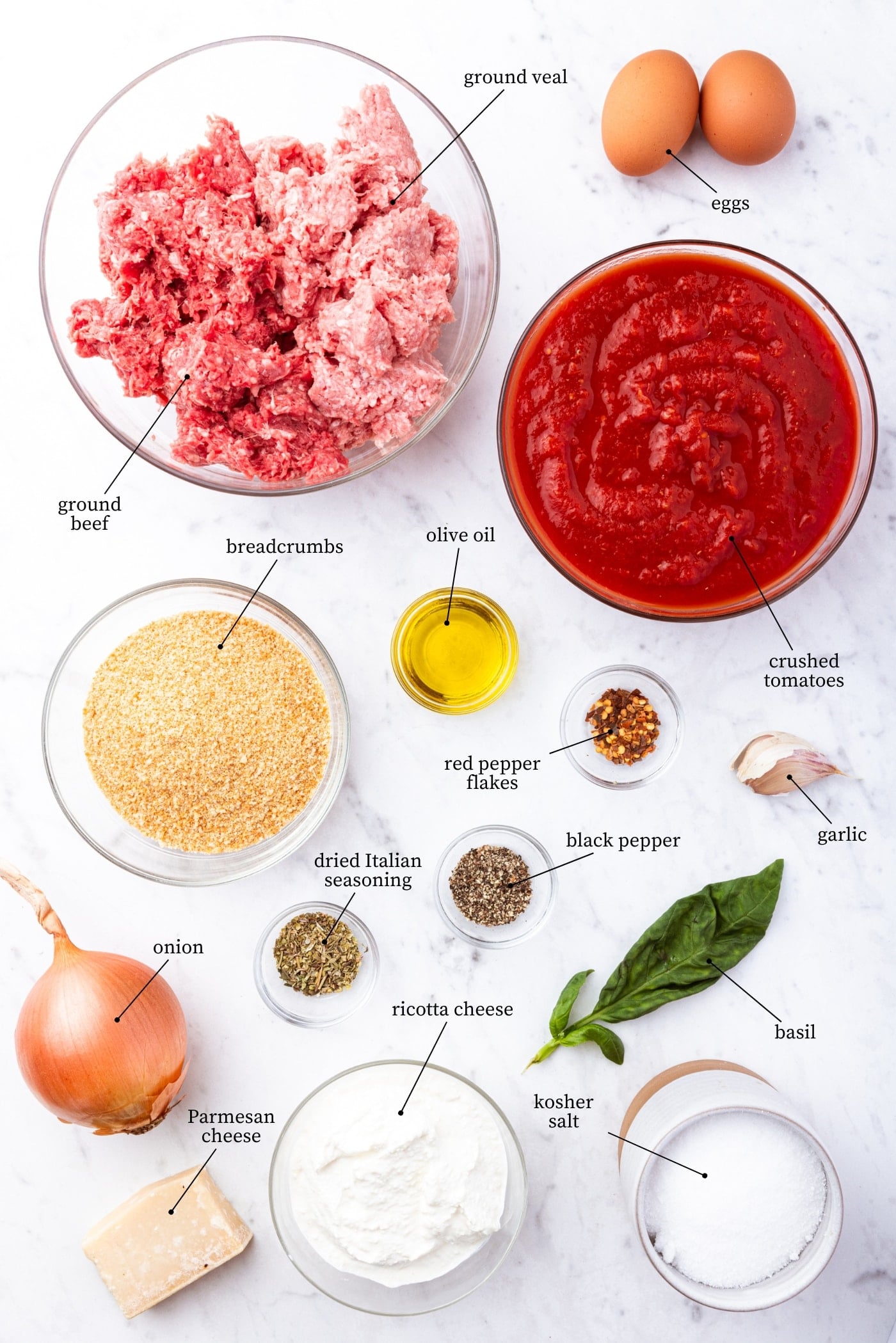 White marble surface filled with all ingredients needed to prepare holiday meatballs including beef and veal, tomato sauce, breadcrumbs, spices, onion, and more.