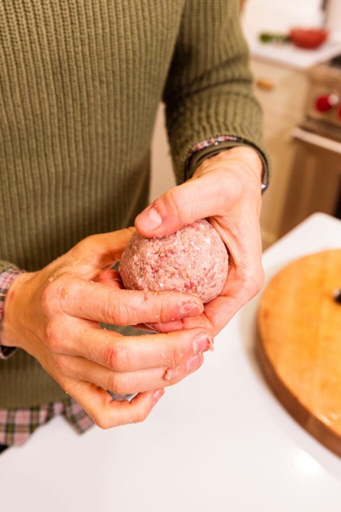 Two hands rolling meat mixture together into a ball to form meatballs.