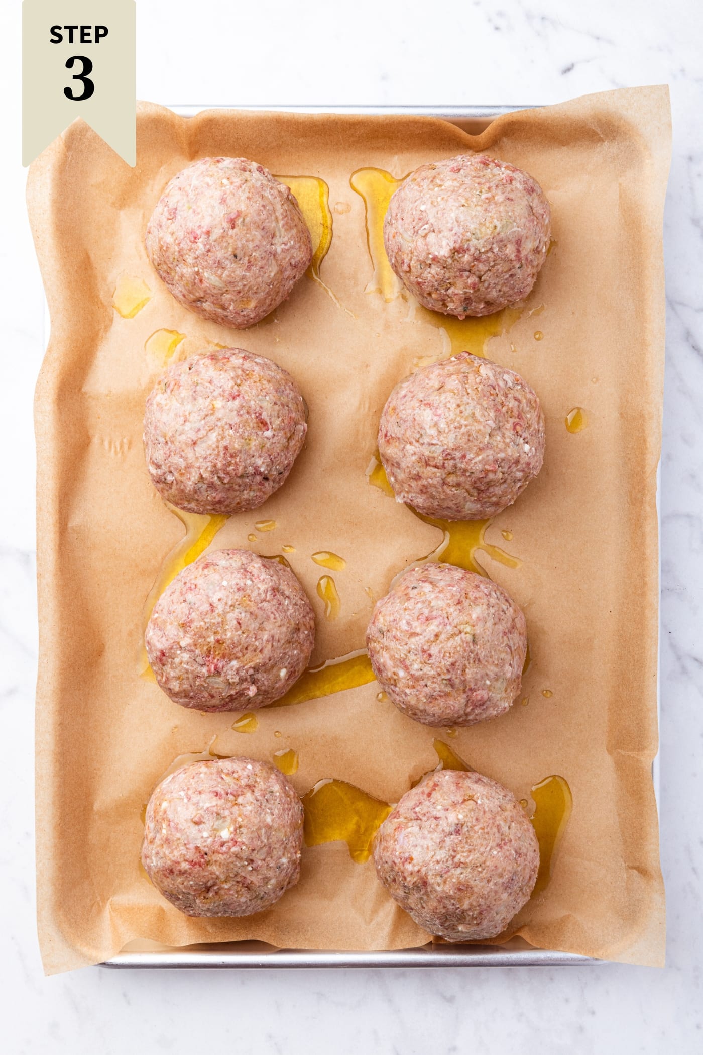White marble surface filled with round meatballs on a baking sheet before being roasted.
