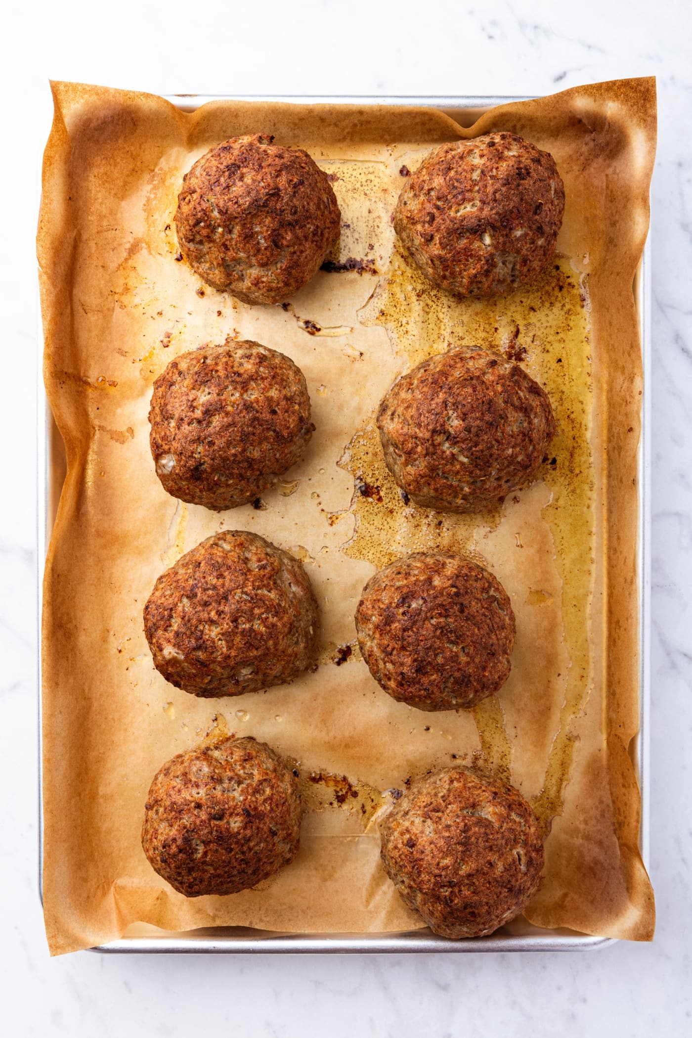 Roasted meatballs resting on a parchment-lined baking sheet after coming out of the oven.