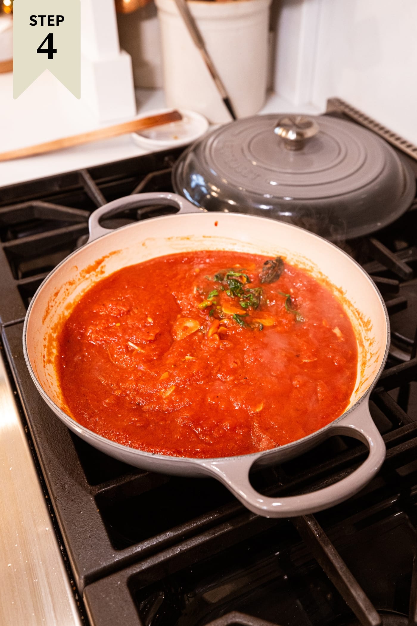 Large round baking dish filled with red sauce simmering on the stovetop.