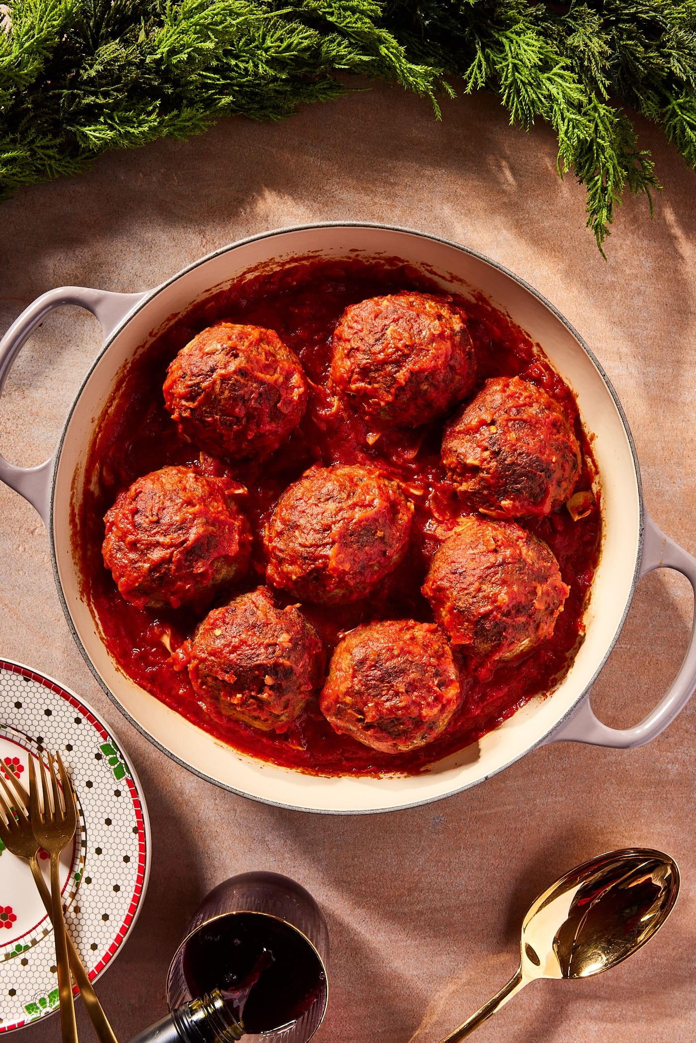 Round baking dish filled with red sauce covered holiday meatballs with Christmas plate to the side.