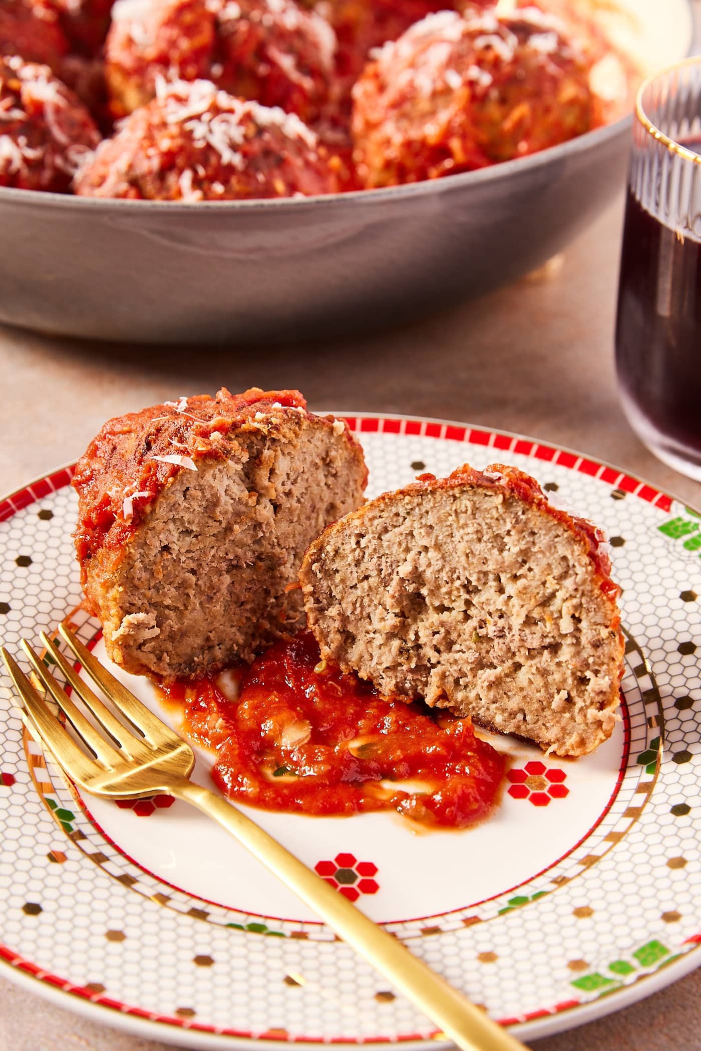 Christmas holiday plate with meatball sliced in half showing interior texture with gold fork to the side.
