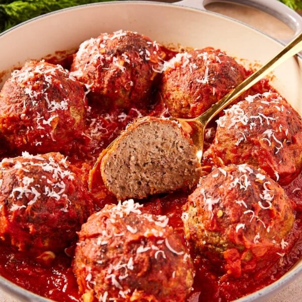 Round baking dish filled with meatballs topped with red tomato sauce with center one sliced in half showing interior texture.