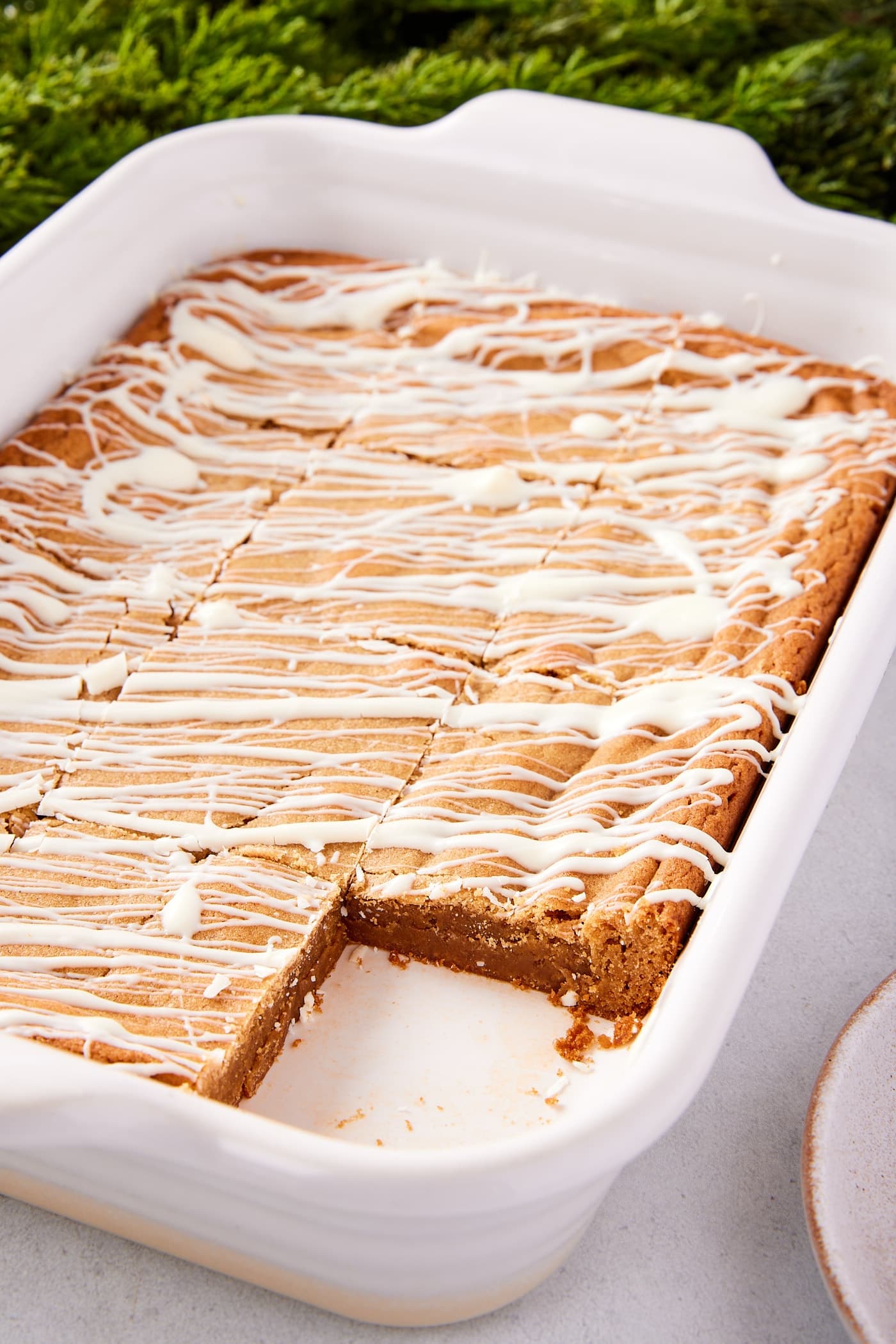 White rectangular baking dish filled with gingerbread blondies with white chocolate drizzled on top with piece missing.