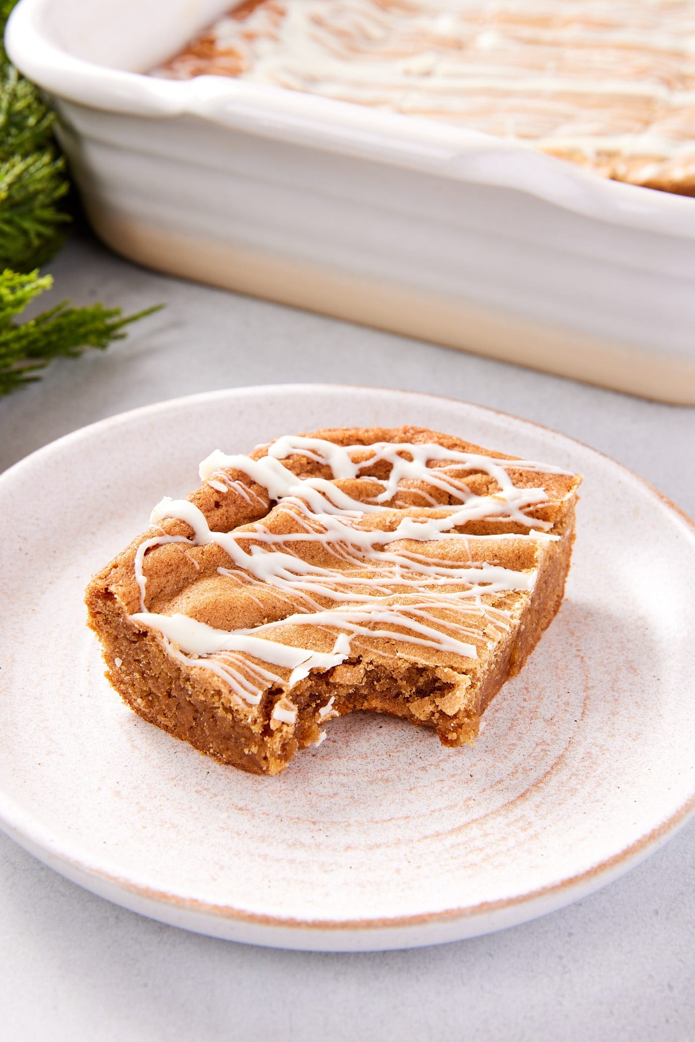 White stoneware plate with slice of gingerbread blondie with white chocolate drizzled on top with bite taken out.