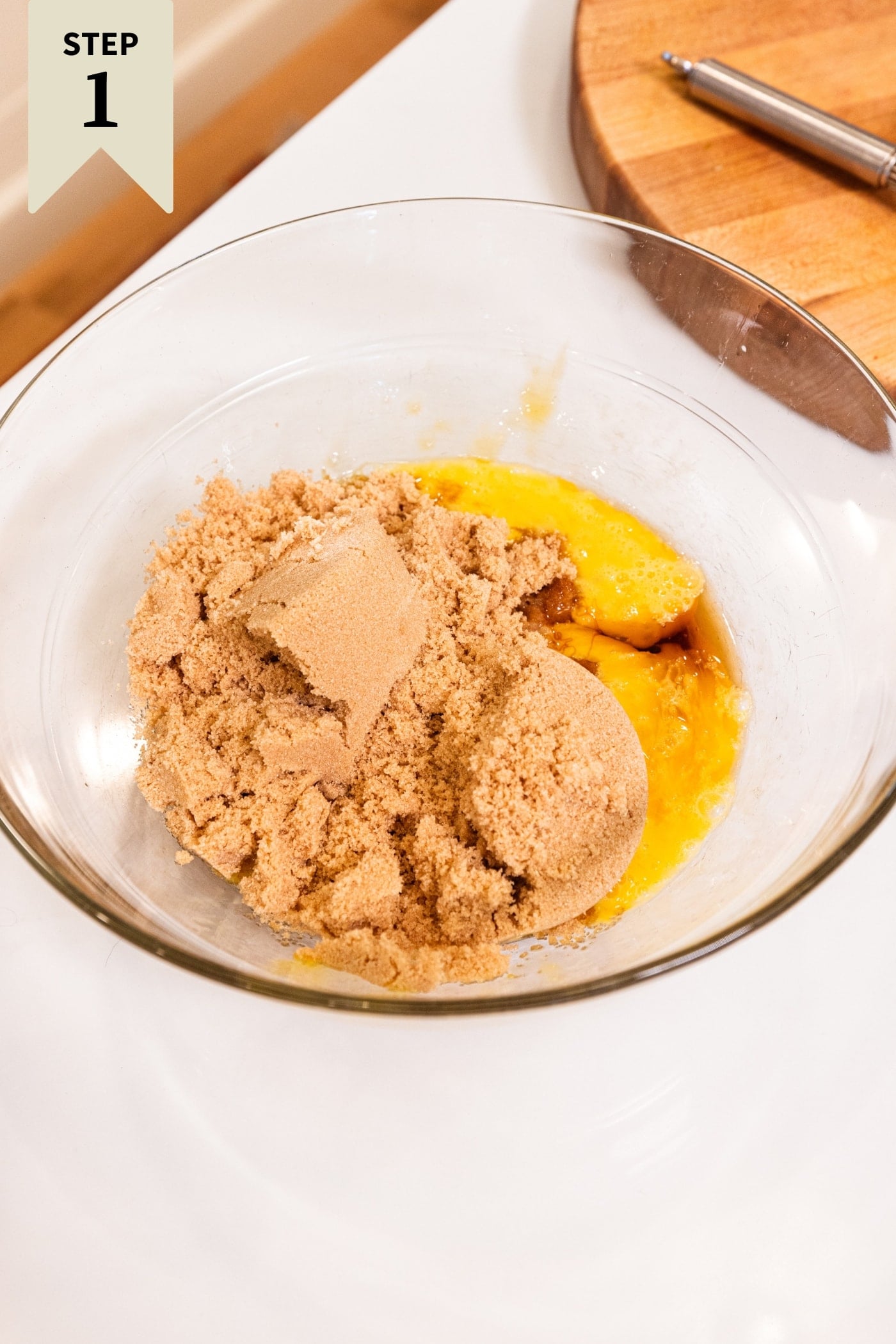 Glass bowl filled with wet ingredients for gingerbread blondies on white surface.