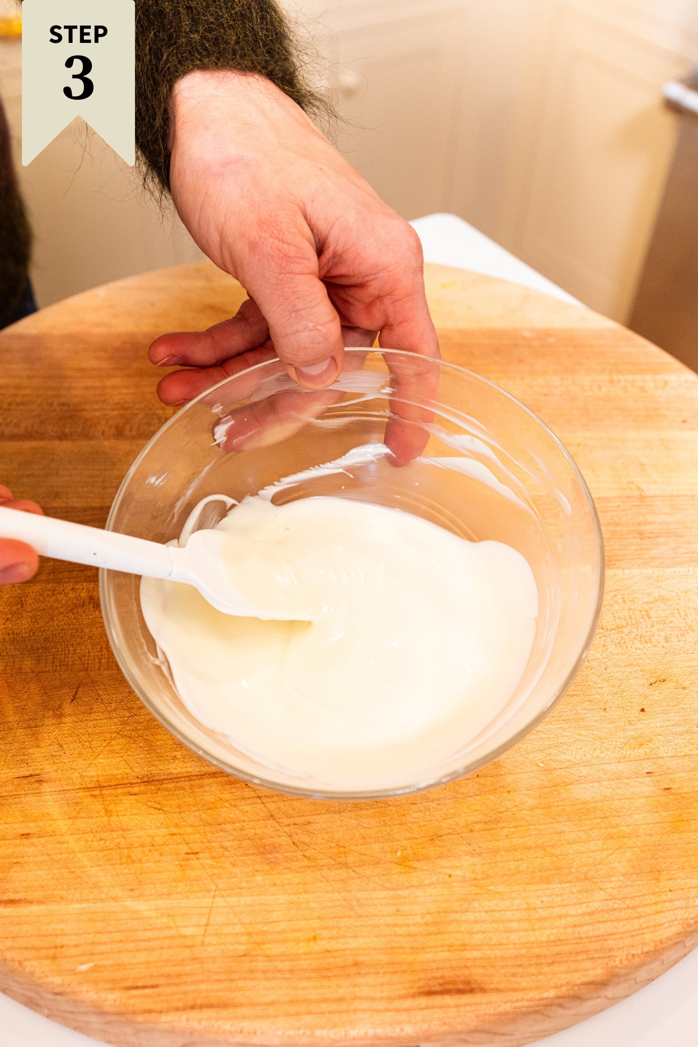 Glass bowl with melted white chocolate with spatula mixing everything together.