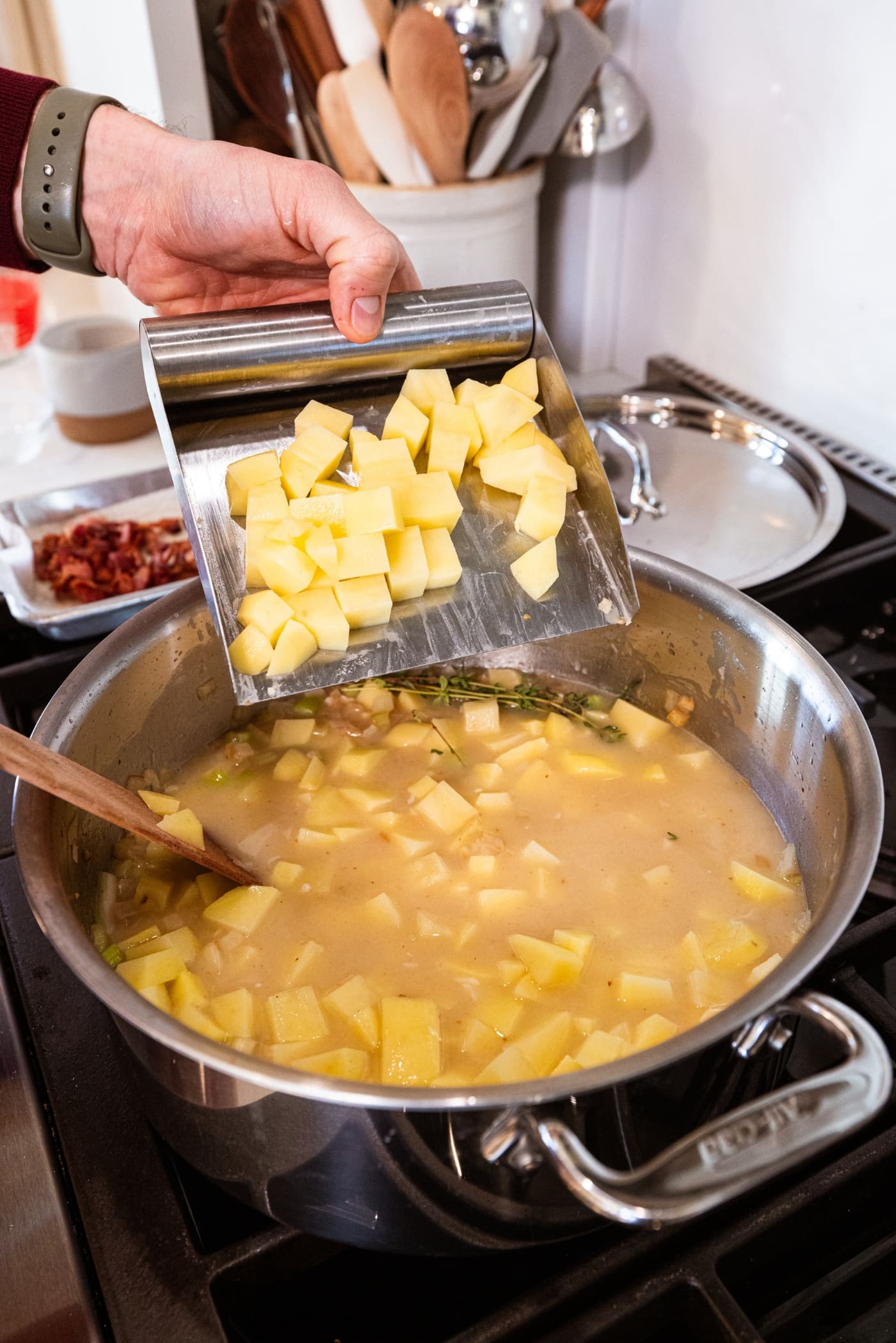 Hand using a scraper to add chopped pieces of potato to a large stockpot already filled with liquid for soup.