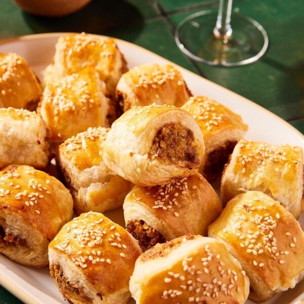 Puff pastry sausage bites stacked on a white platter on green tiles.