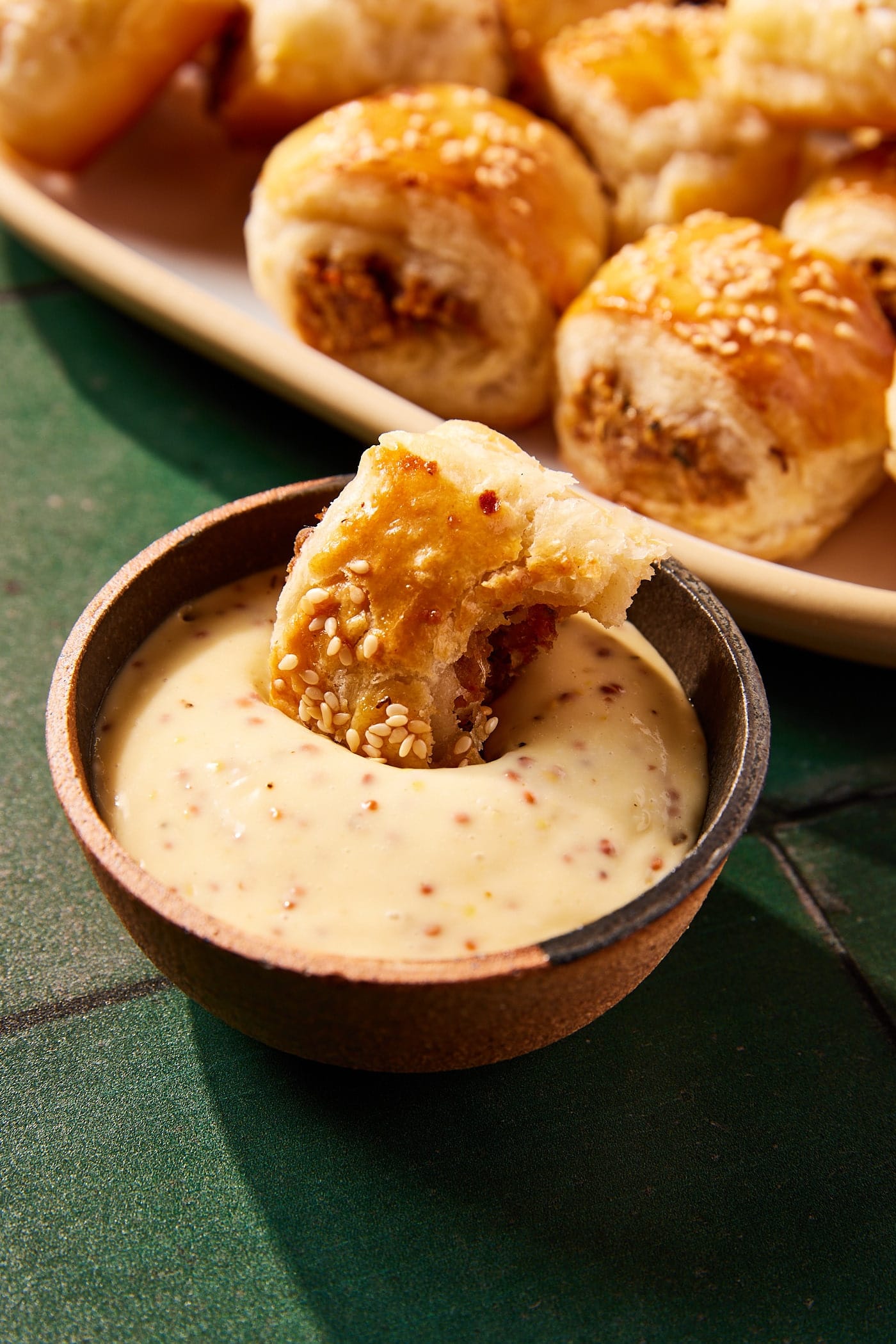 Small bowl filled with mustard mayonnaise sauce with puff pastry sausage bite with bite taken out dipping into sauce.