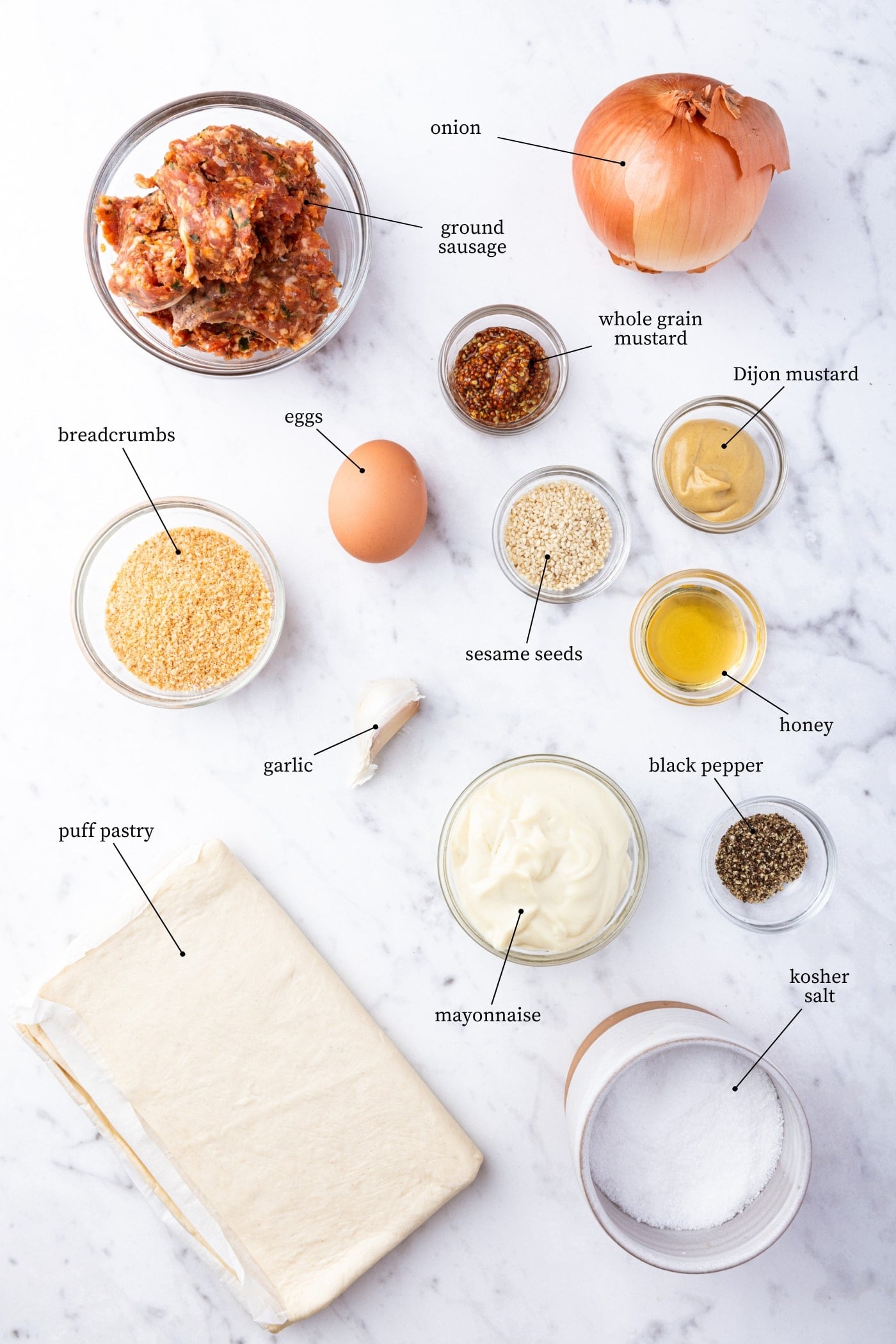 White marble surface with ingredients needed for puff pastry sausage bites including spices, mustard, mayonnaise, puff pastry, and more.