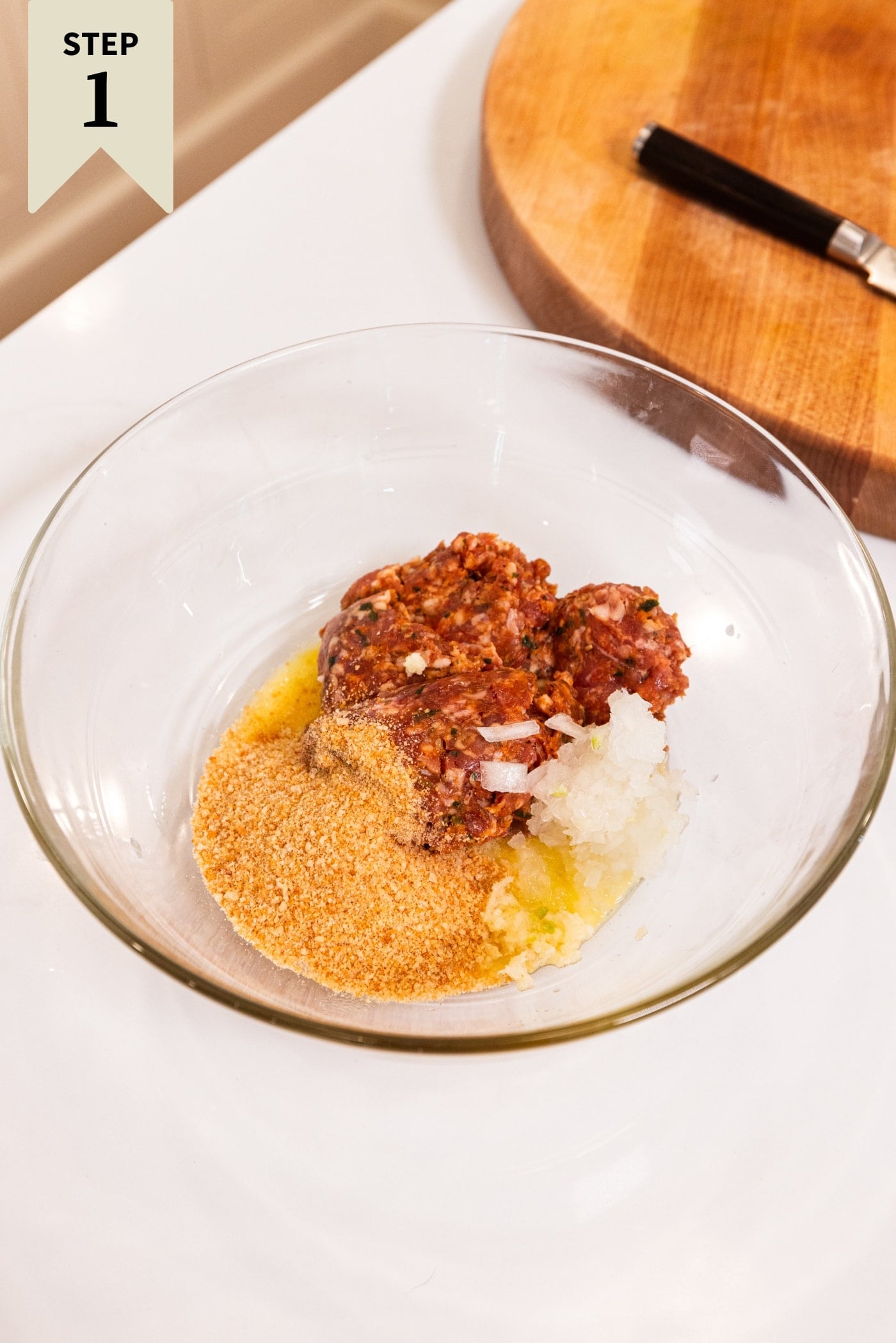 Glass bowl with puff pastry sausage bites ingredients including raw meat, breadcrumbs, spices, and more in a glass bowl.