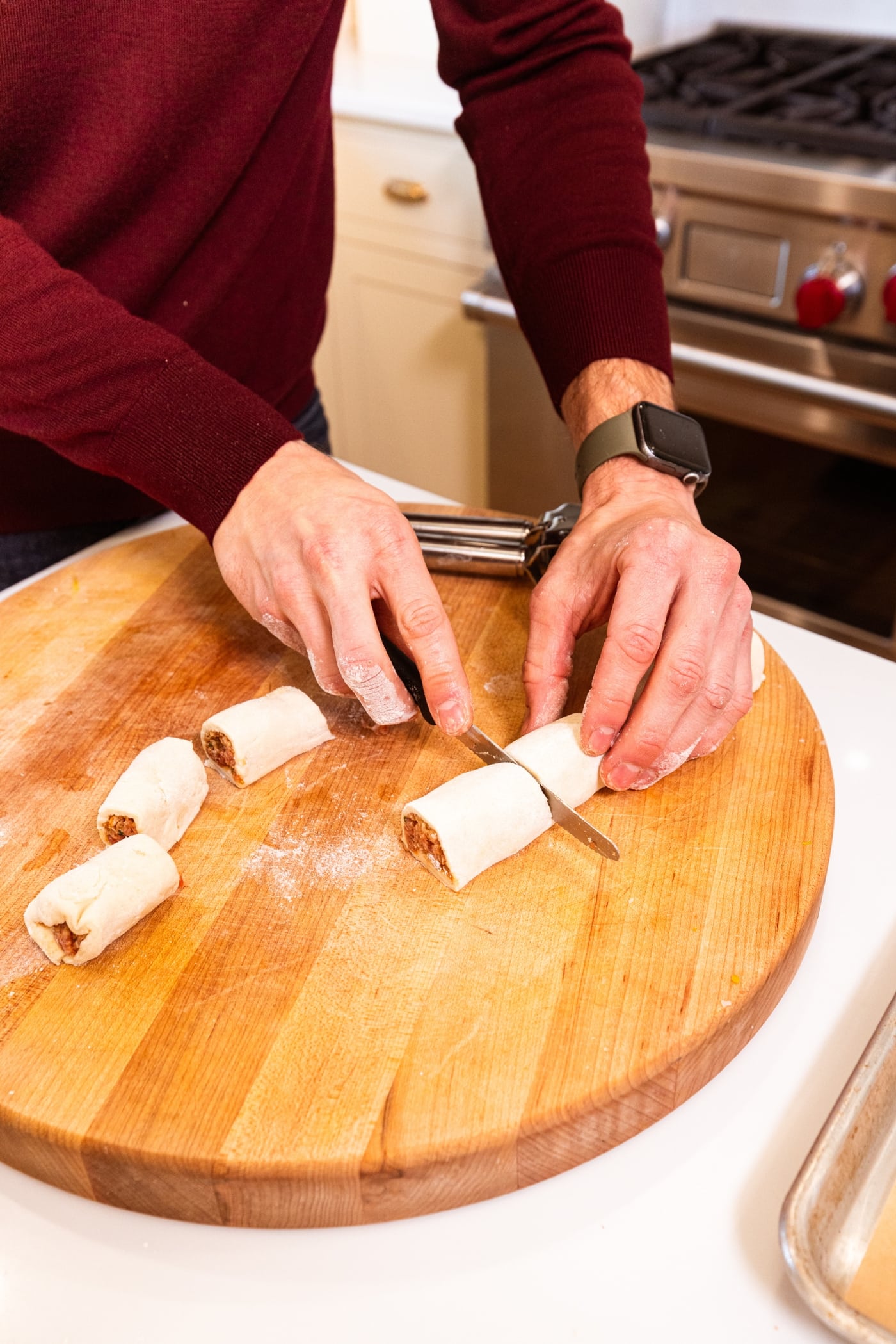 Hands using knife to slice puff pastry log into eight pieces on wood cutting board.
