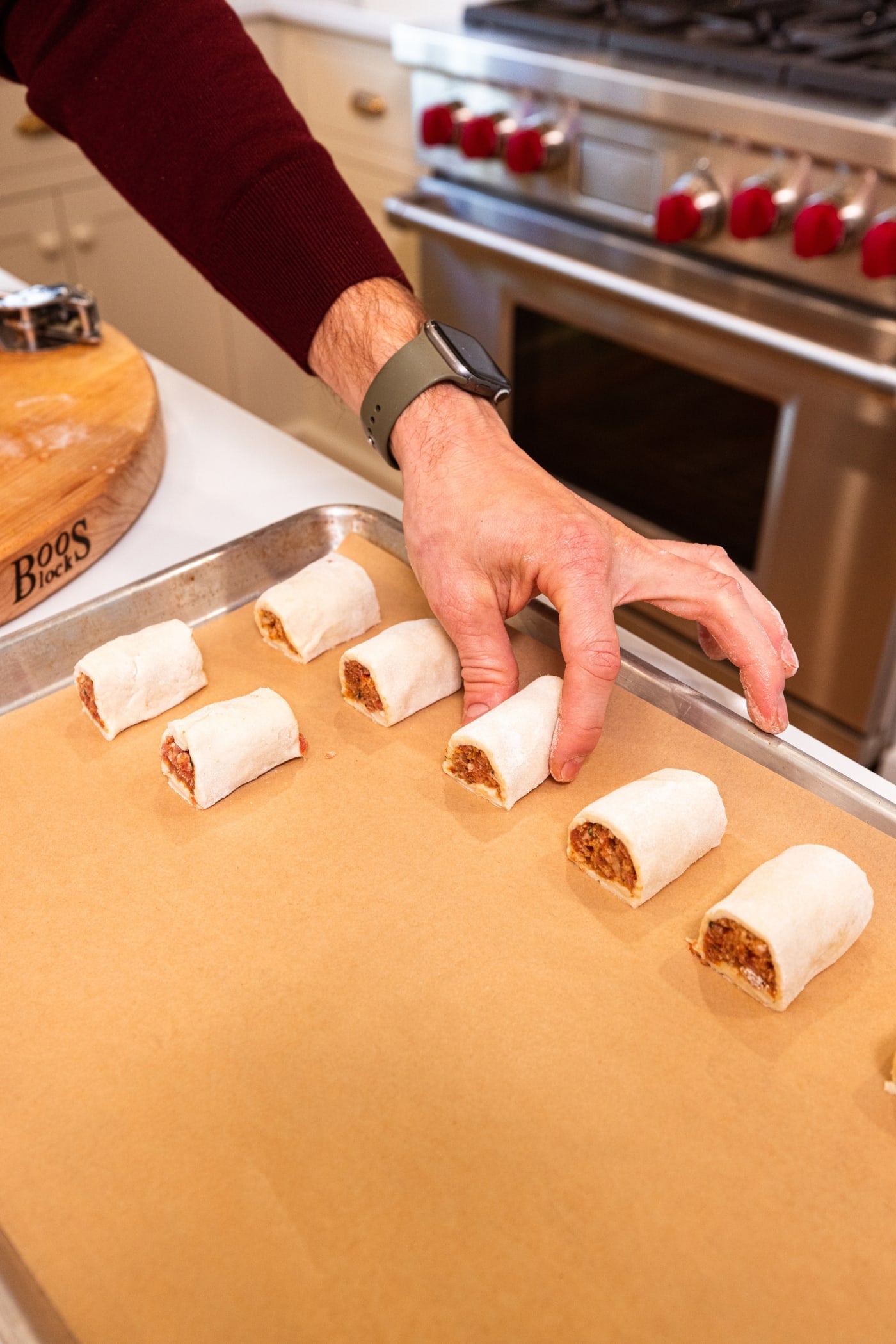 Hand placing pieces of puff pastry sausage bites on parchment-lined baking sheet before baking.